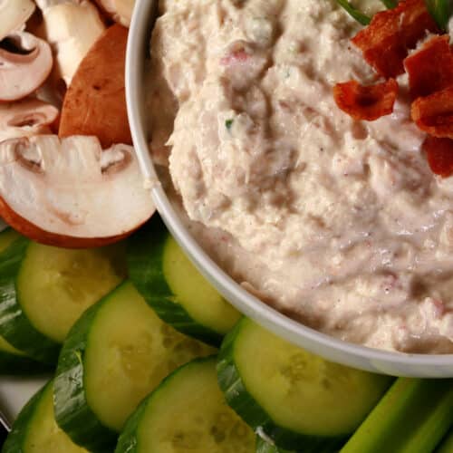 A bowl of smoky keto cold crab dip, topped with bacon and surrounded by vegetables to dip.