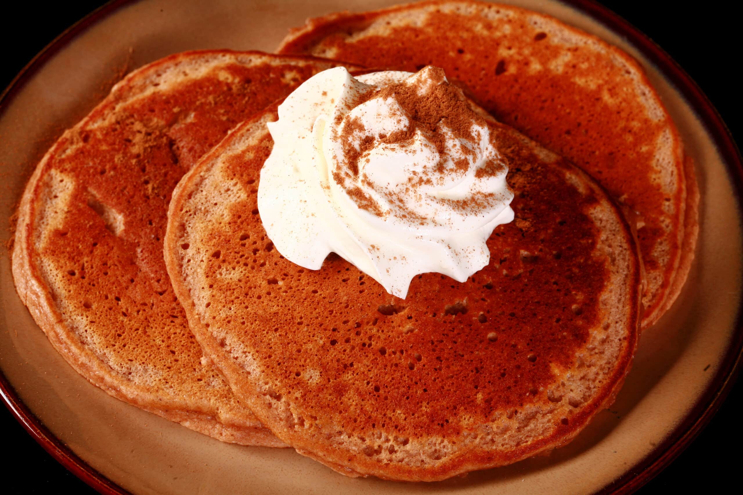 A plate of keto gingerbread pancakes, topped with whipped cream.