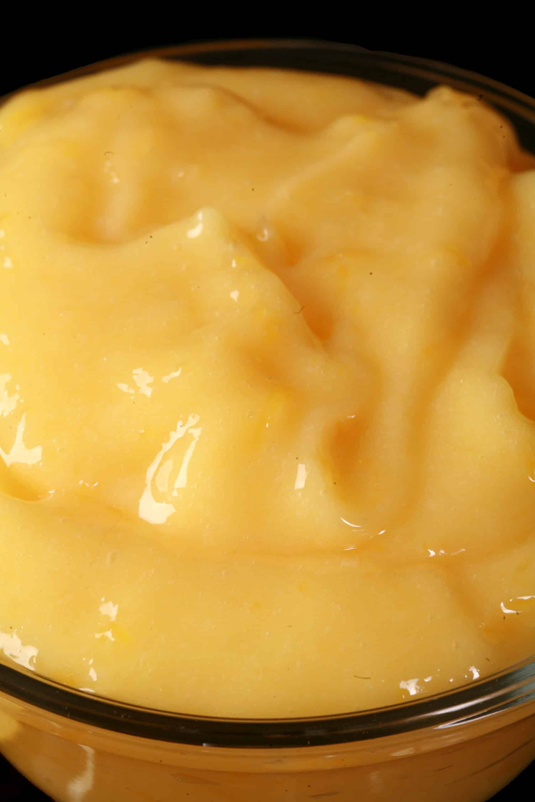 A small bowl of sugar free lemon curd, along with lemon slices and a spoon of curd.