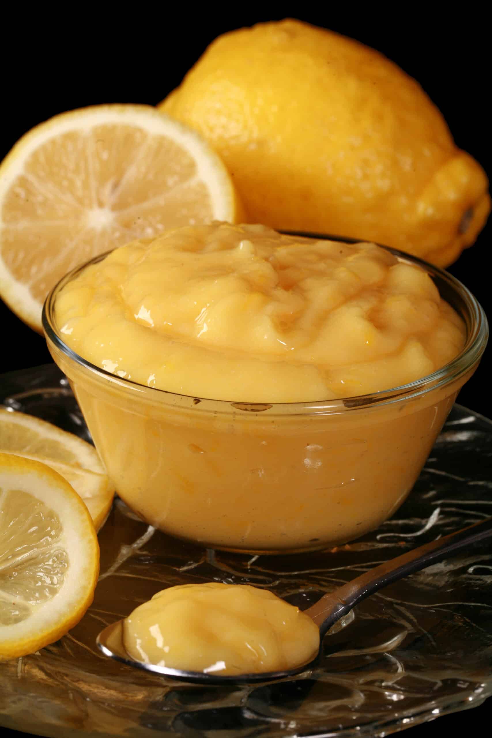 A small bowl of low carb lemon curd, along with lemon slices and a spoon of curd.