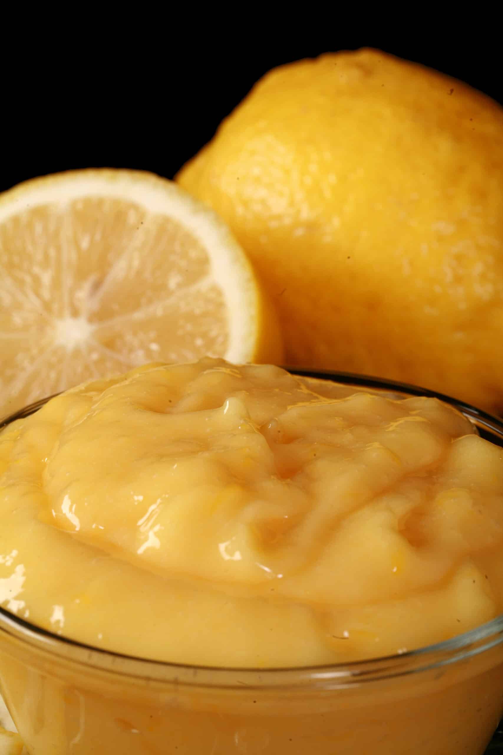 A small bowl of keto lemon curd, along with lemon slices and a spoon of curd.