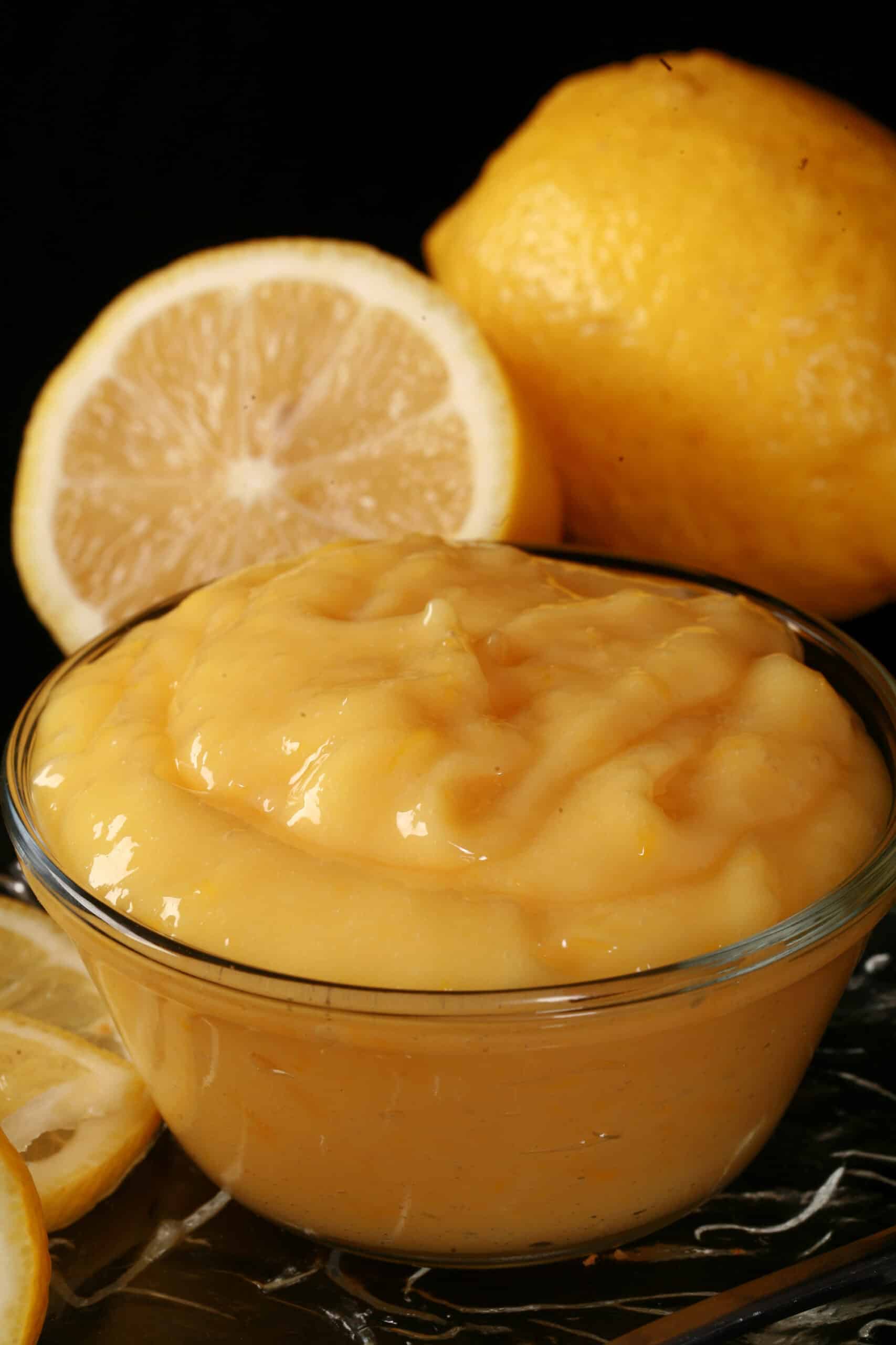 A small bowl of sugar free lemon curd, along with lemon slices and a spoon of curd.