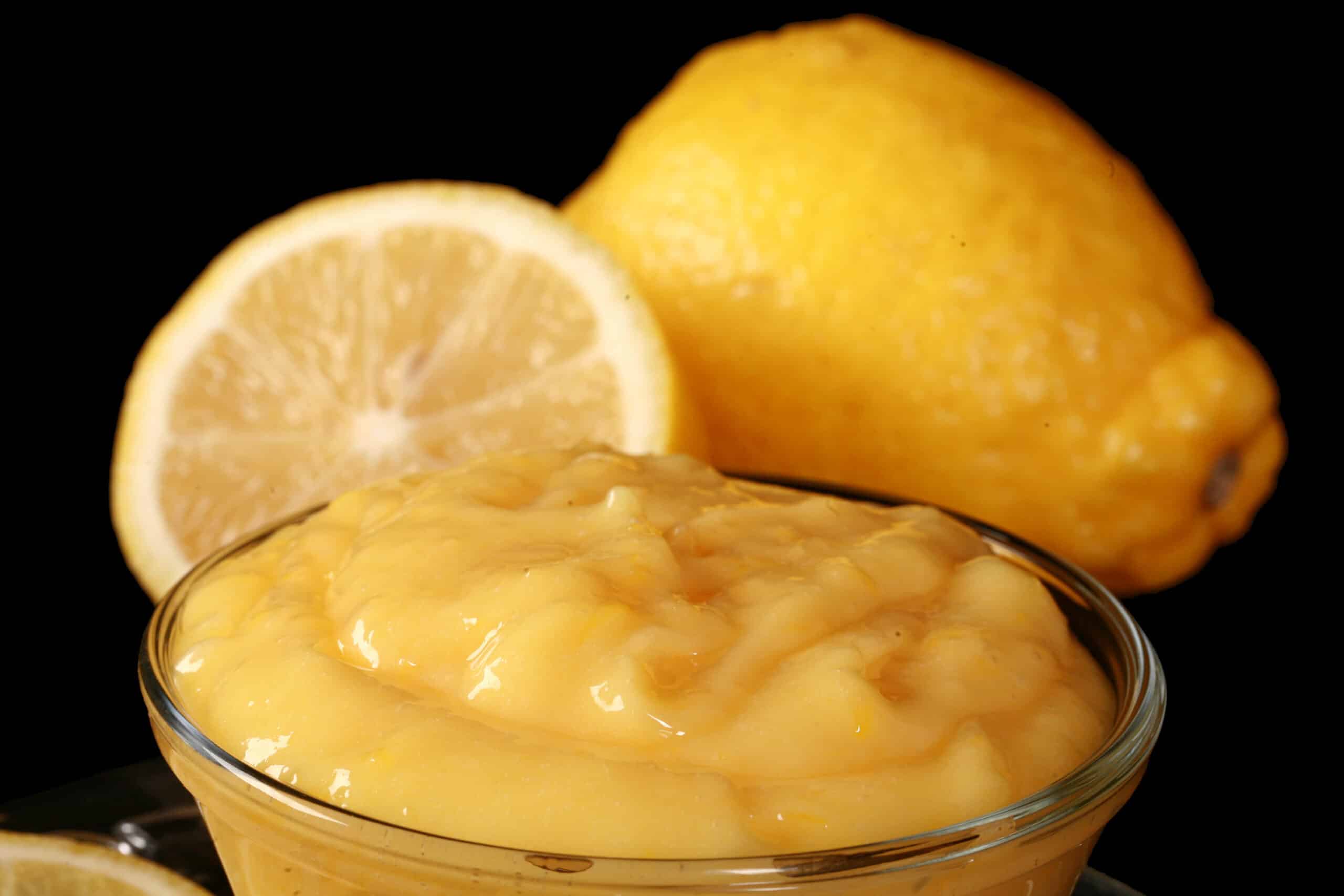 A small bowl of low carb lemon curd, along with lemon slices and a spoon of curd.