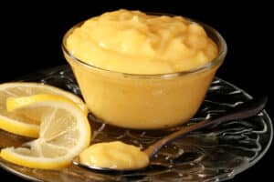 A small bowl of keto lemon curd, along with lemon slices and a spoon of curd.