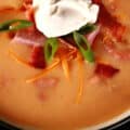 A bowl of keto loaded perogy soup, garnished with kielbasa, bacon, cheddar cheese, sour cream, and green onions.