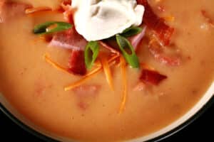 A bowl of keto loaded perogy soup, garnished with kielbasa, bacon, cheddar cheese, sour cream, and green onions.