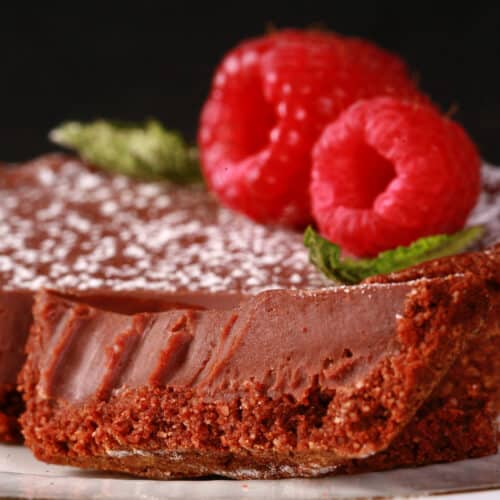 A Keto Mini Chocolate Tart garnished with powdered sweetener, fresh raspberries and mint leaves.