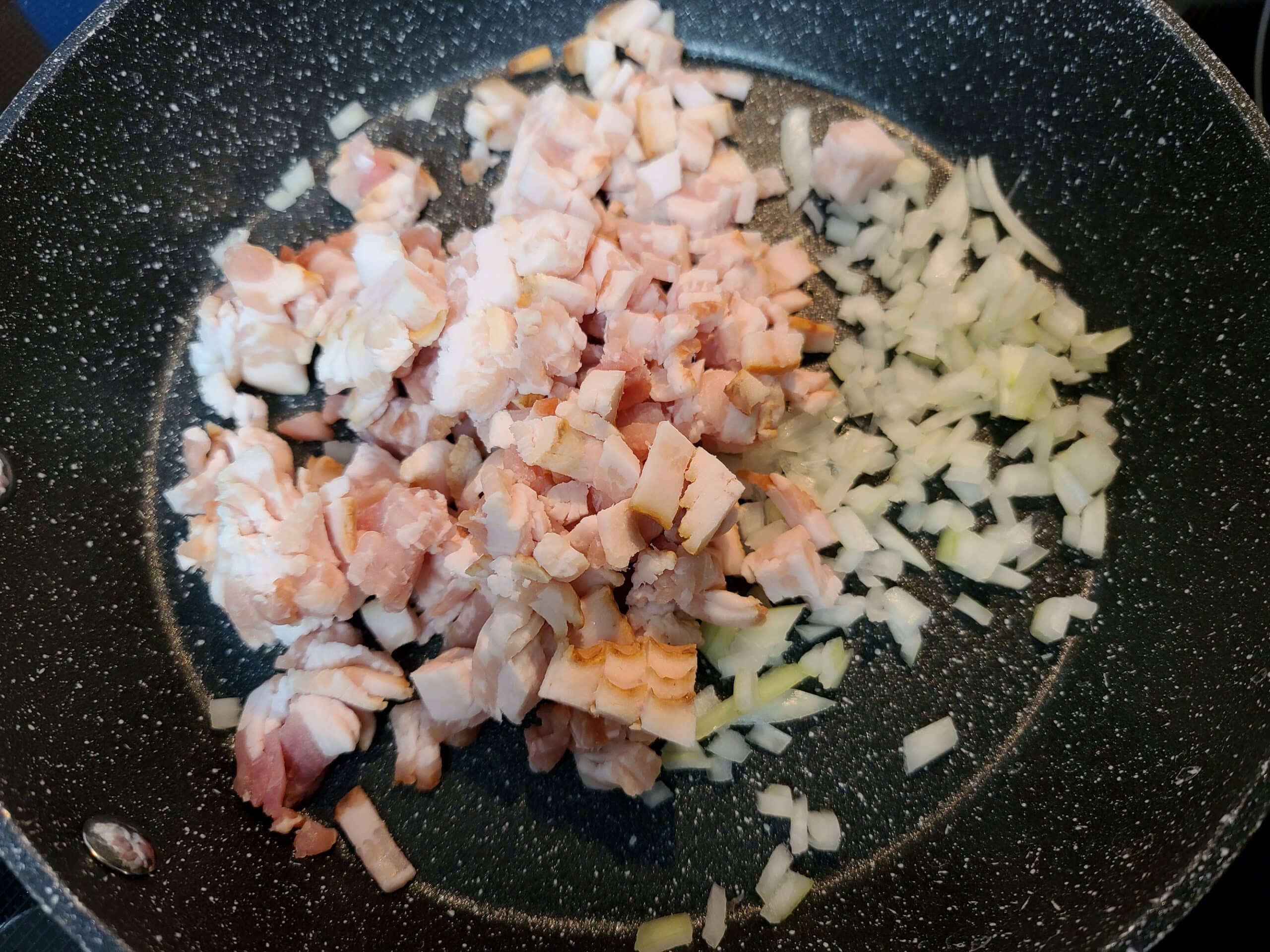 A pan of chopped bacon and onions cooking.