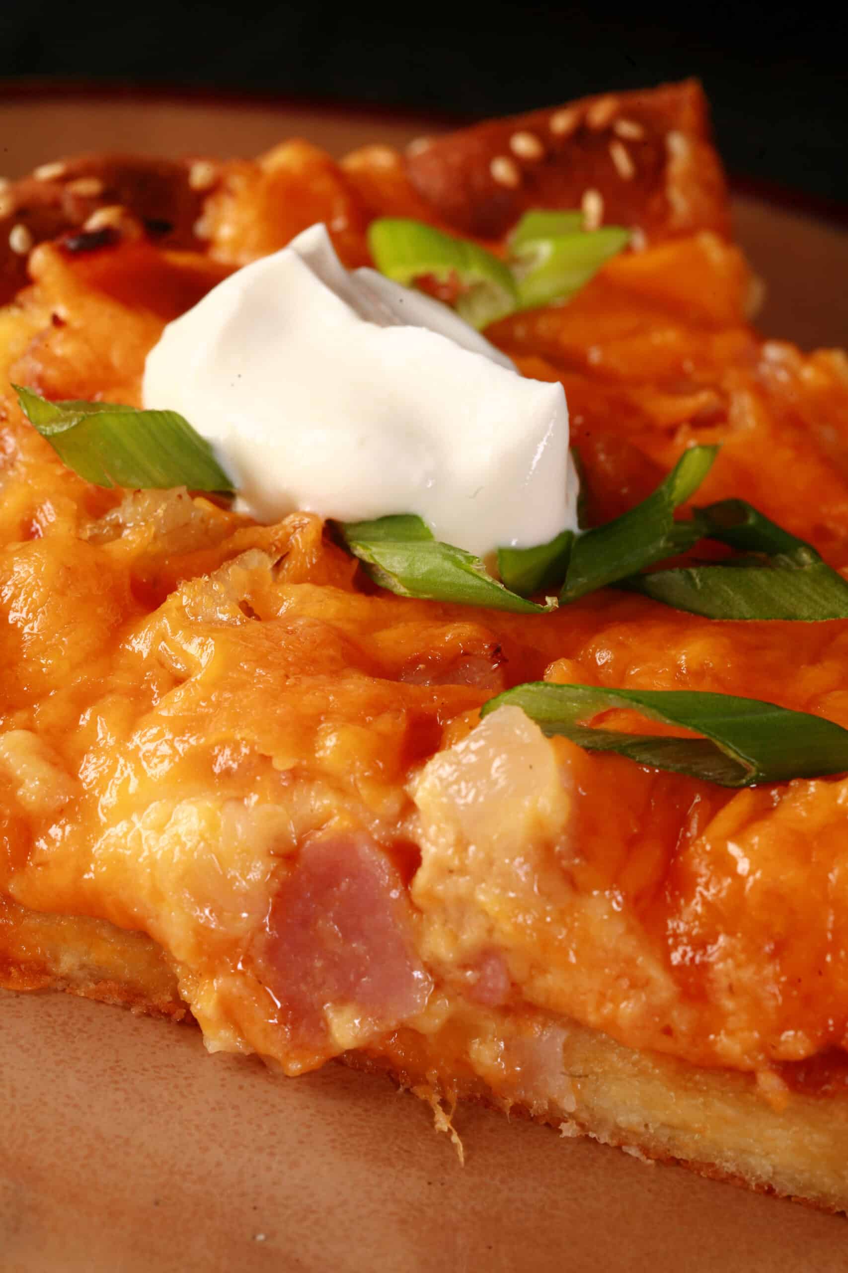 A keto perogy pizza topped with sour cream and sliced green onions.