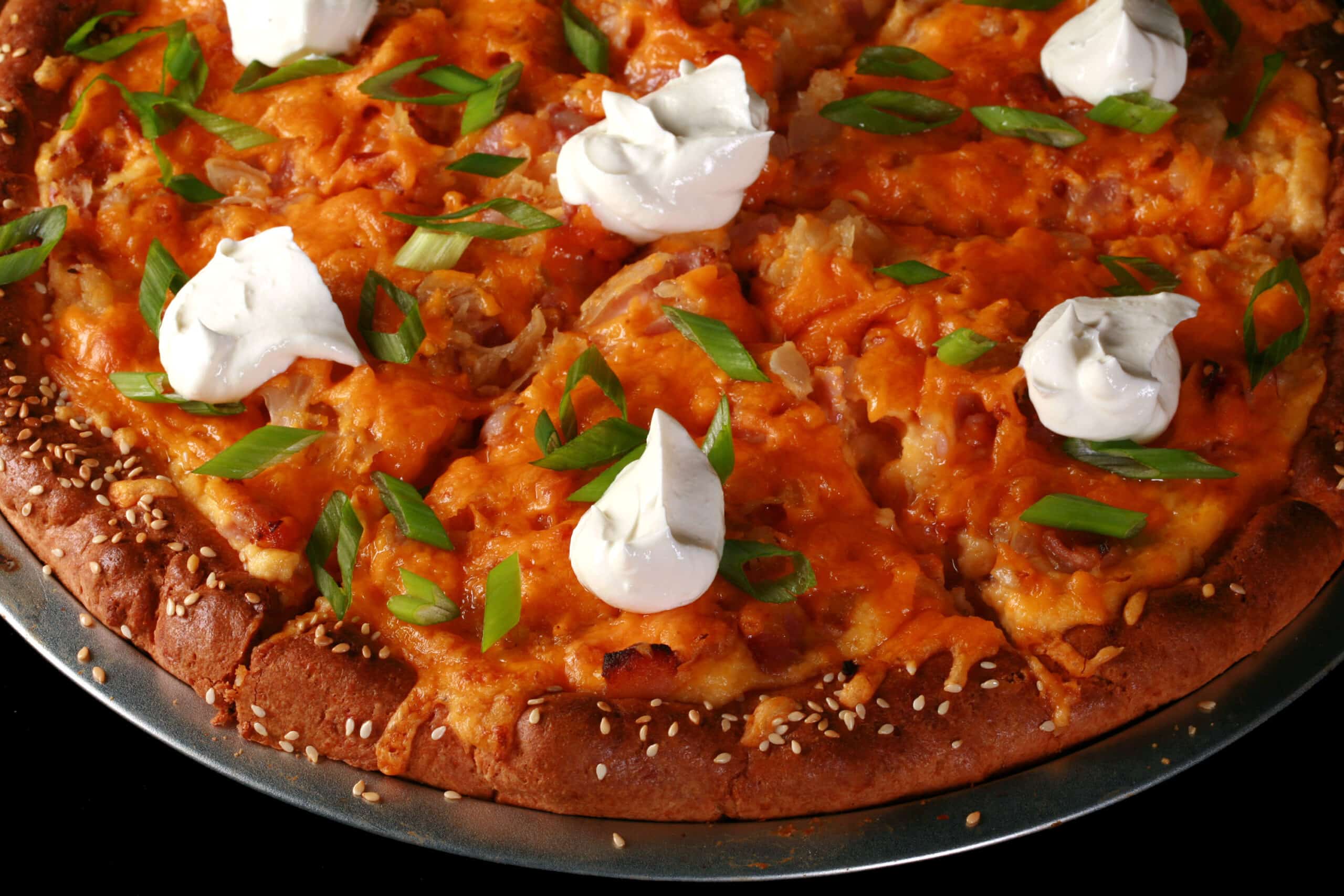 A keto pierogi pizza topped with sour cream and sliced green onions.