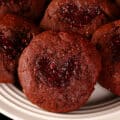 A plate of low carb chocolate thumbprint cookies. The indentations are heart shaped and filled with sugar free raspberry jam.