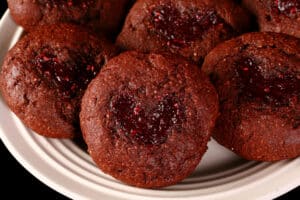 A plate of low carb chocolate thumbprint cookies. The indentations are heart shaped and filled with sugar free raspberry jam.