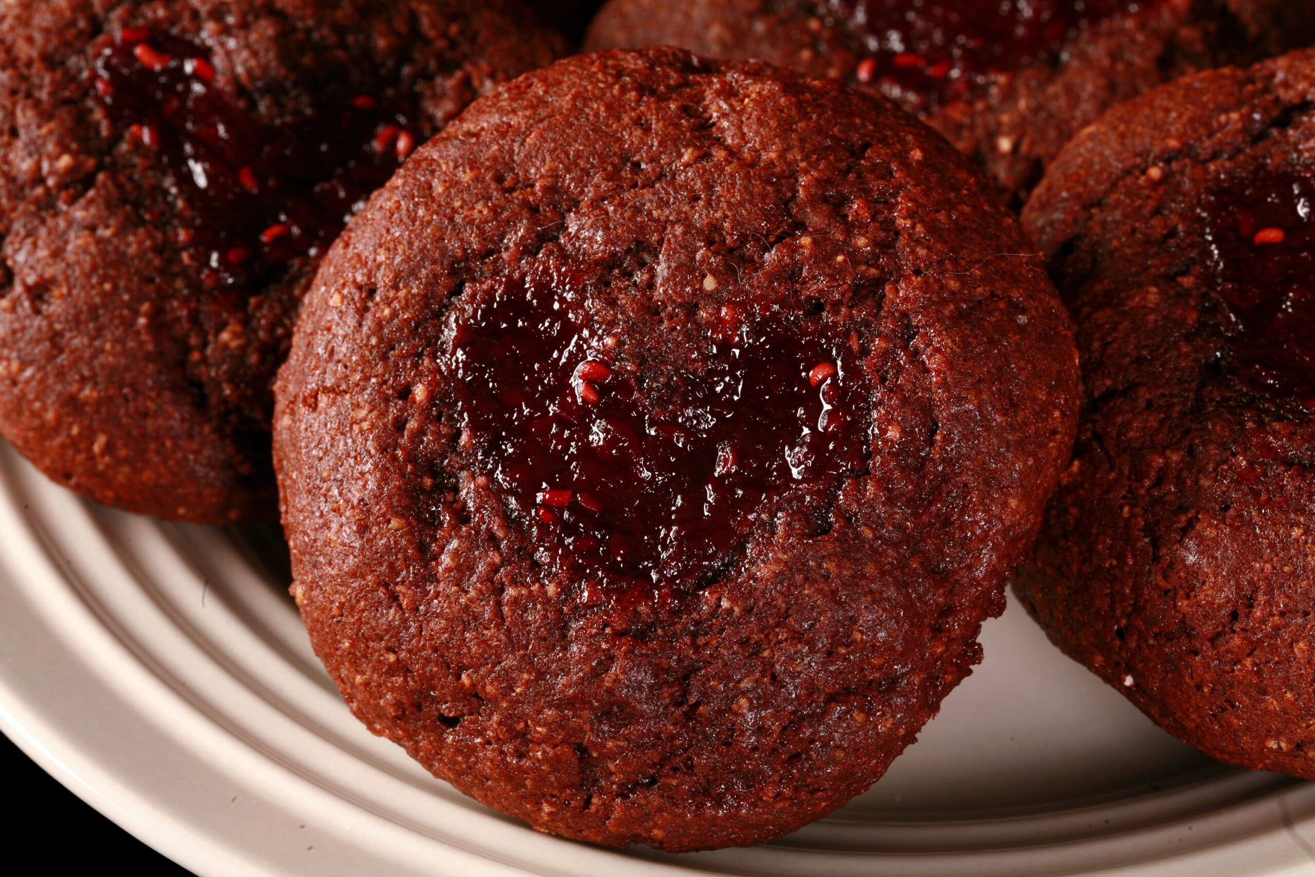 A plate of keto chocolate thumbprint cookies. The indentations are heart shaped and filled with sugar free raspberry jam.