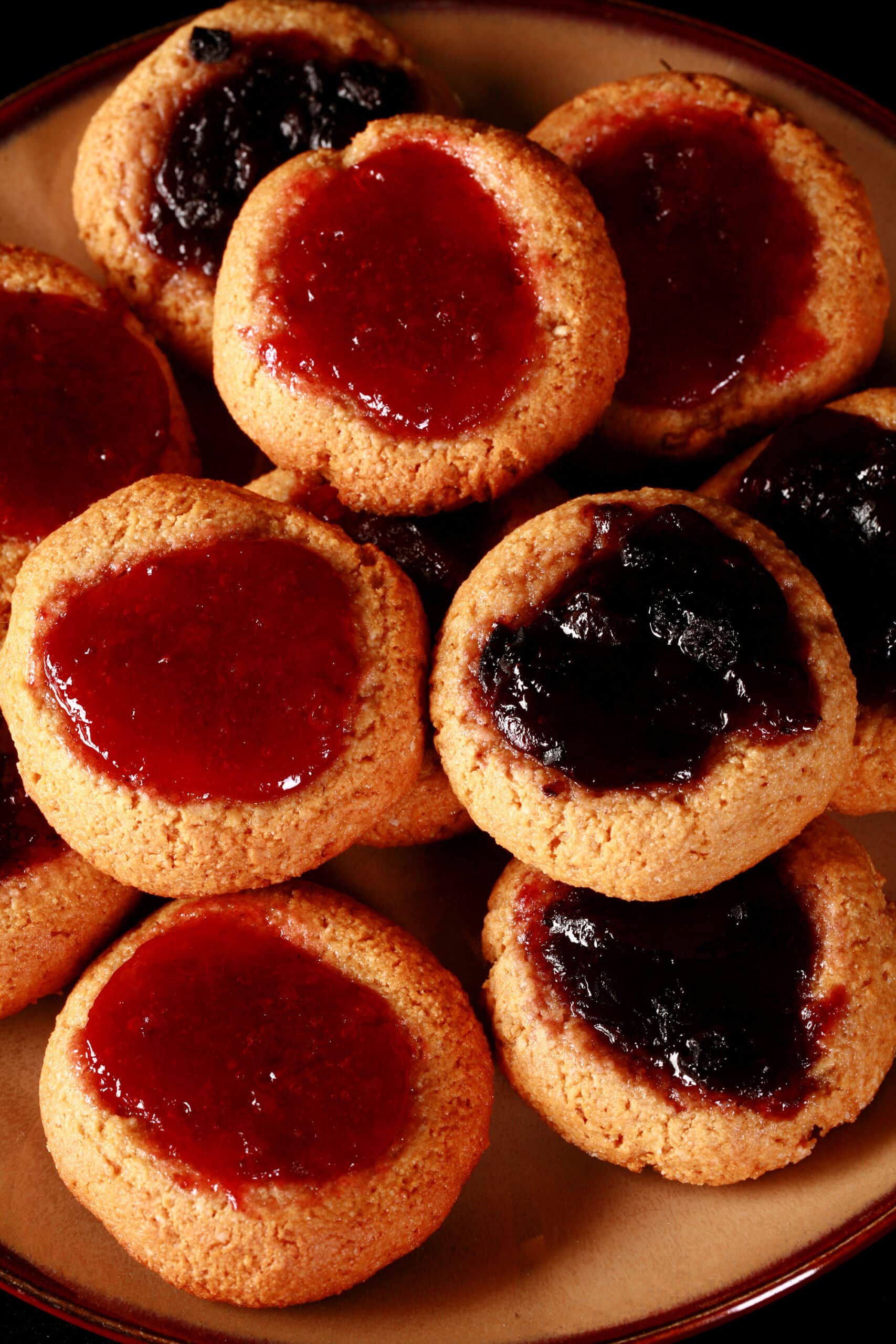 A plate of keto peanut butter thumbprint cookies, topped with sugar free blueberry and sugar free strawberry jam.