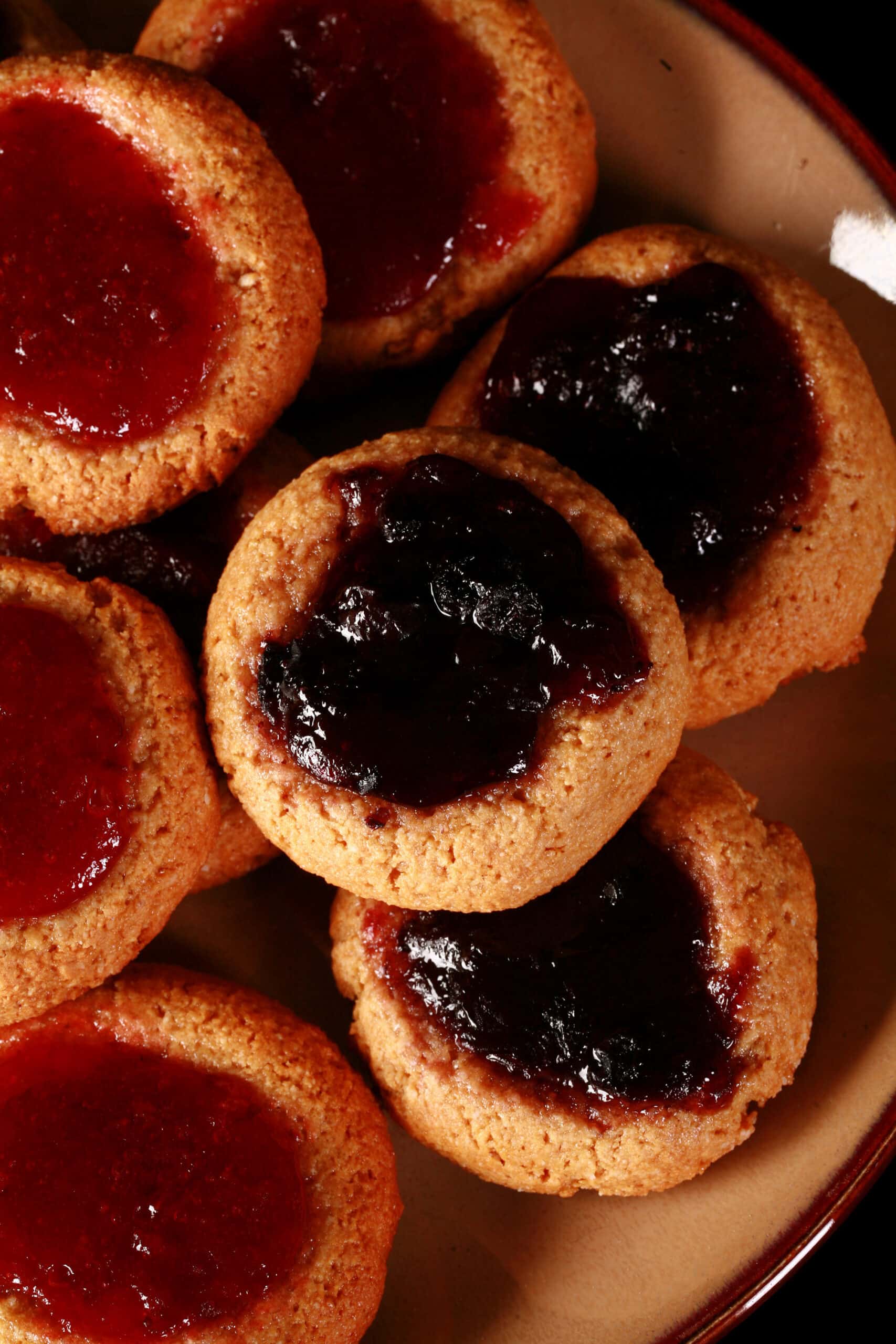 A plate of low carb peanut butter thumbprint cookies, topped with sugar free blueberry and sugar free strawberry jam.