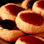 A plate of keto peanut butter thumbprint cookies, topped with sugar free blueberry and sugar free strawberry jam.