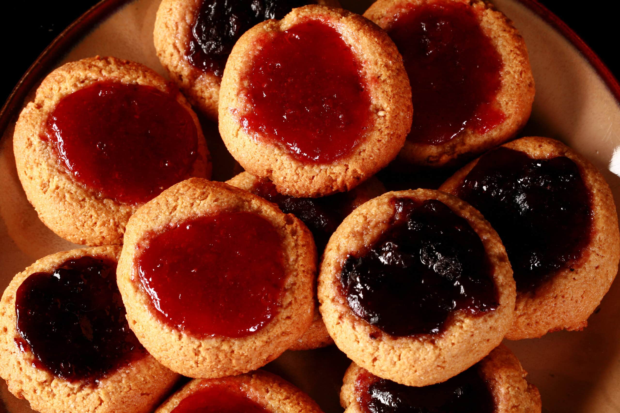 A plate of keto peanut butter and jelly cookies, topped with sugar free blueberry and sugar free strawberry jam.
