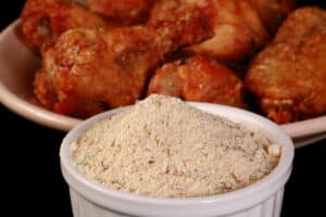 A a small bowl of Mediterranean seasoning, in front of a plate of Greek dry rub wings.