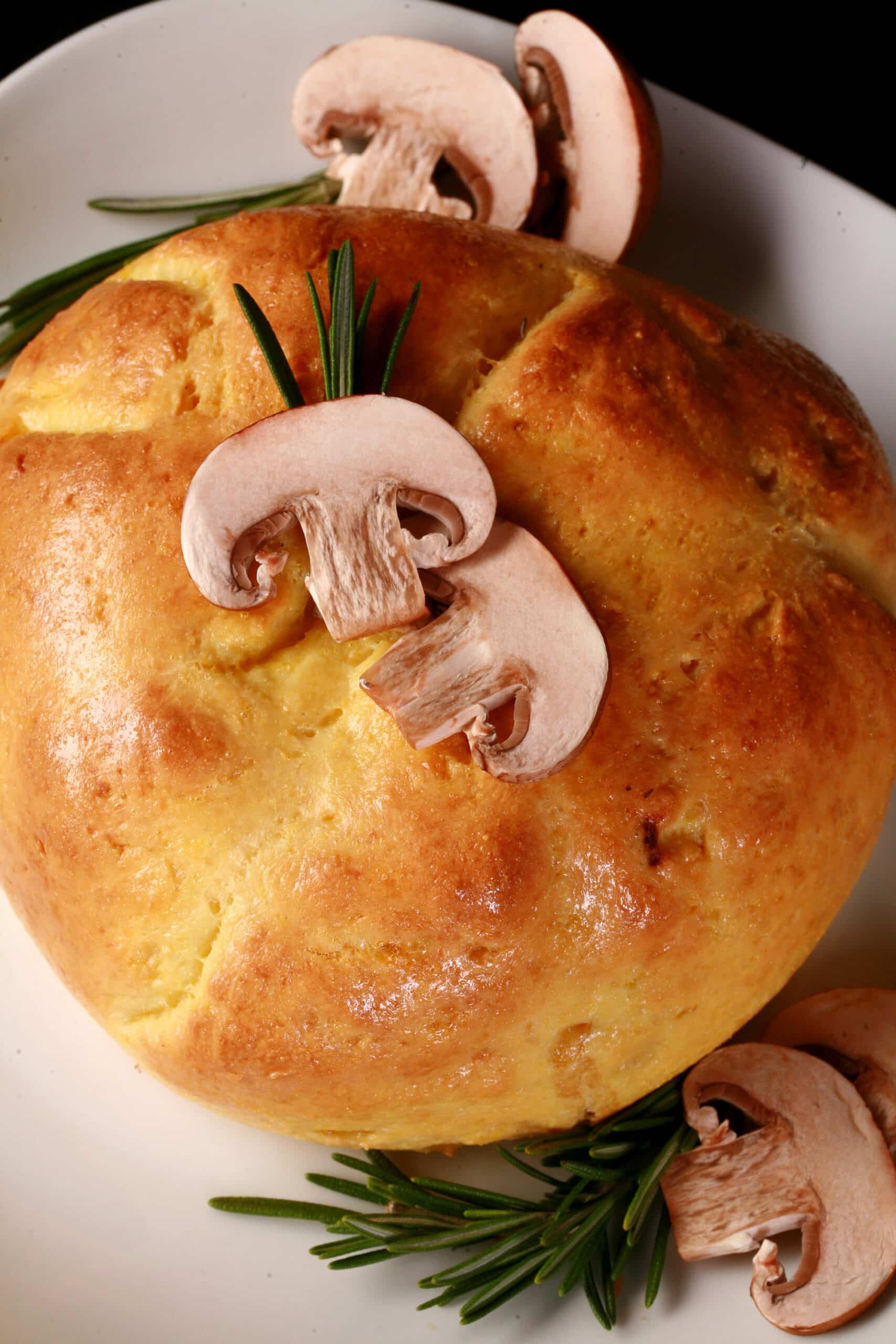 A whole pastry wrapped Keto Brie en Croute, topped with sliced mushrooms and a rosemary sprig.
