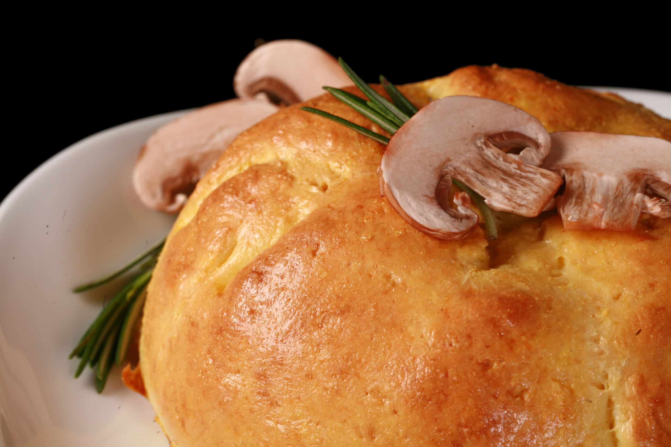 A whole pastry wrapped Keto Brie en Croute, topped with sliced mushrooms and a rosemary sprig.