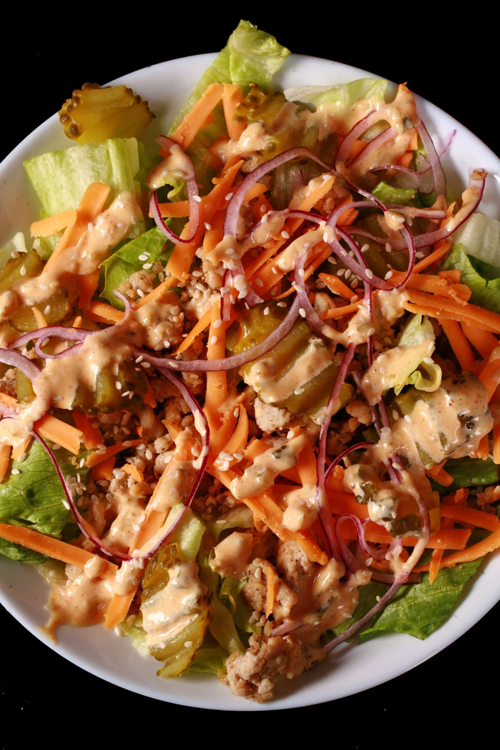 A bowl of keto big mac salad, with iceberg lettuce, ground beef, cheese, pickles, onions, and low carb big mac sauce.