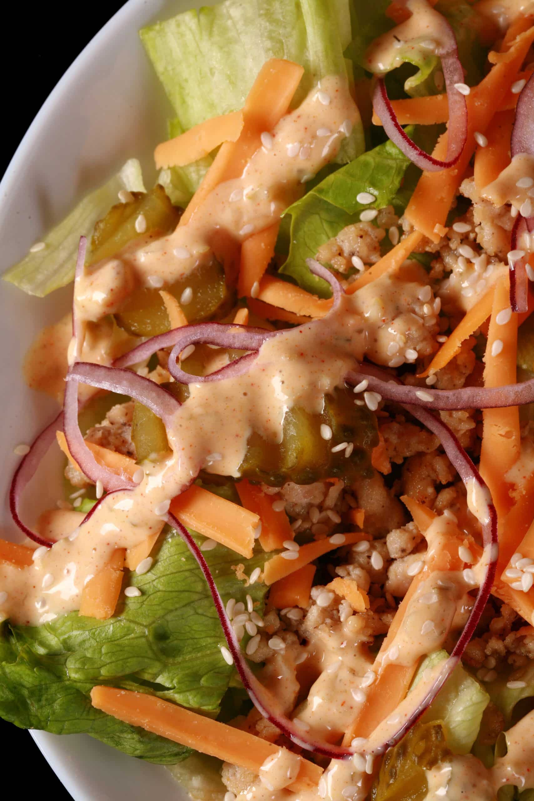 A bowl of keto big mac salad, with iceberg lettuce, ground beef, cheese, pickles, onions, and low carb big mac sauce.