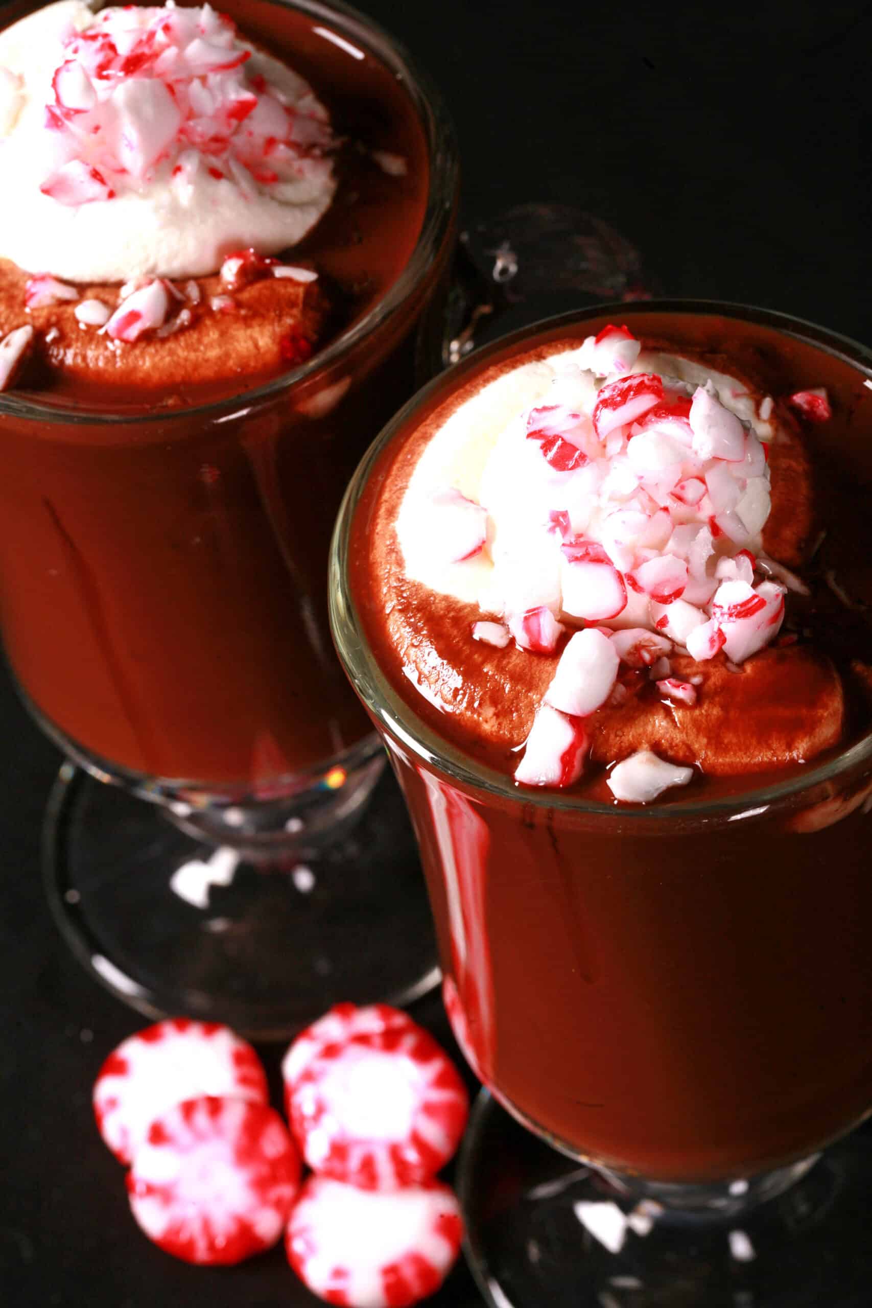 2 glass mugs of keto peppermint hot cocoa topped with whipped cream and crushed sugar free peppermint candies.