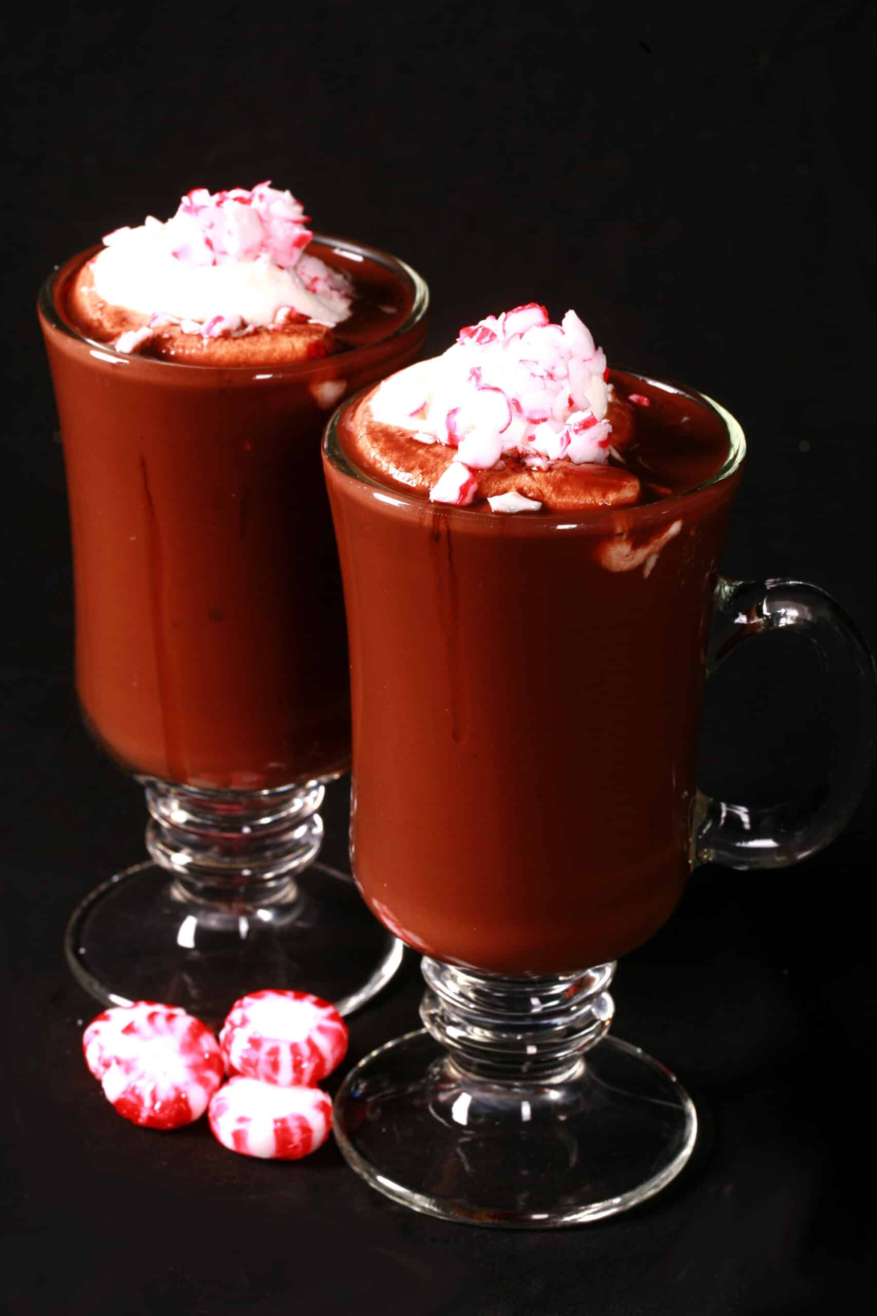 2 glass mugs of low carb peppermint hot cocoa topped with whipped cream and crushed sugar free peppermint candies.