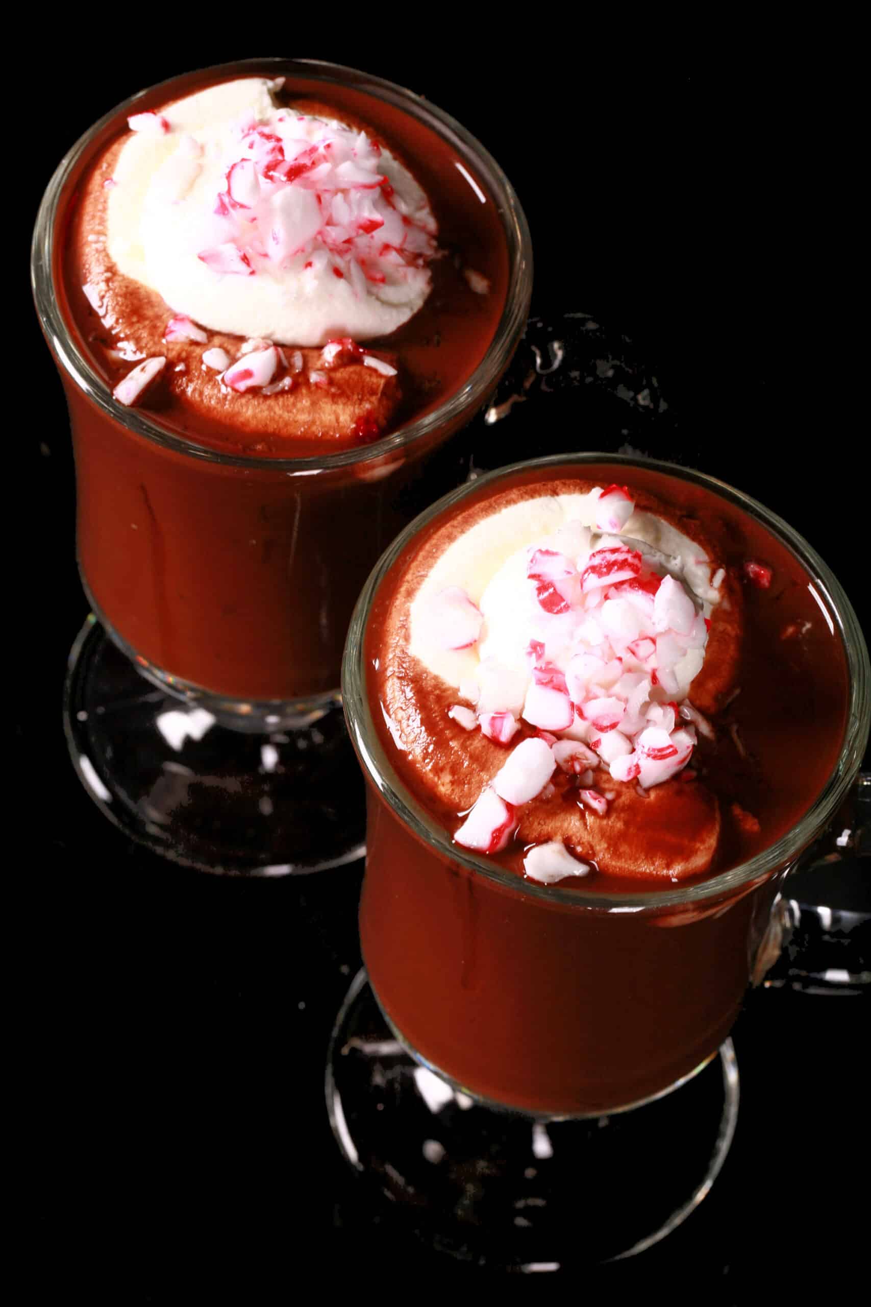 2 glass mugs of keto peppermint hot chocolate topped with whipped cream and crushed sugar free peppermint candies.