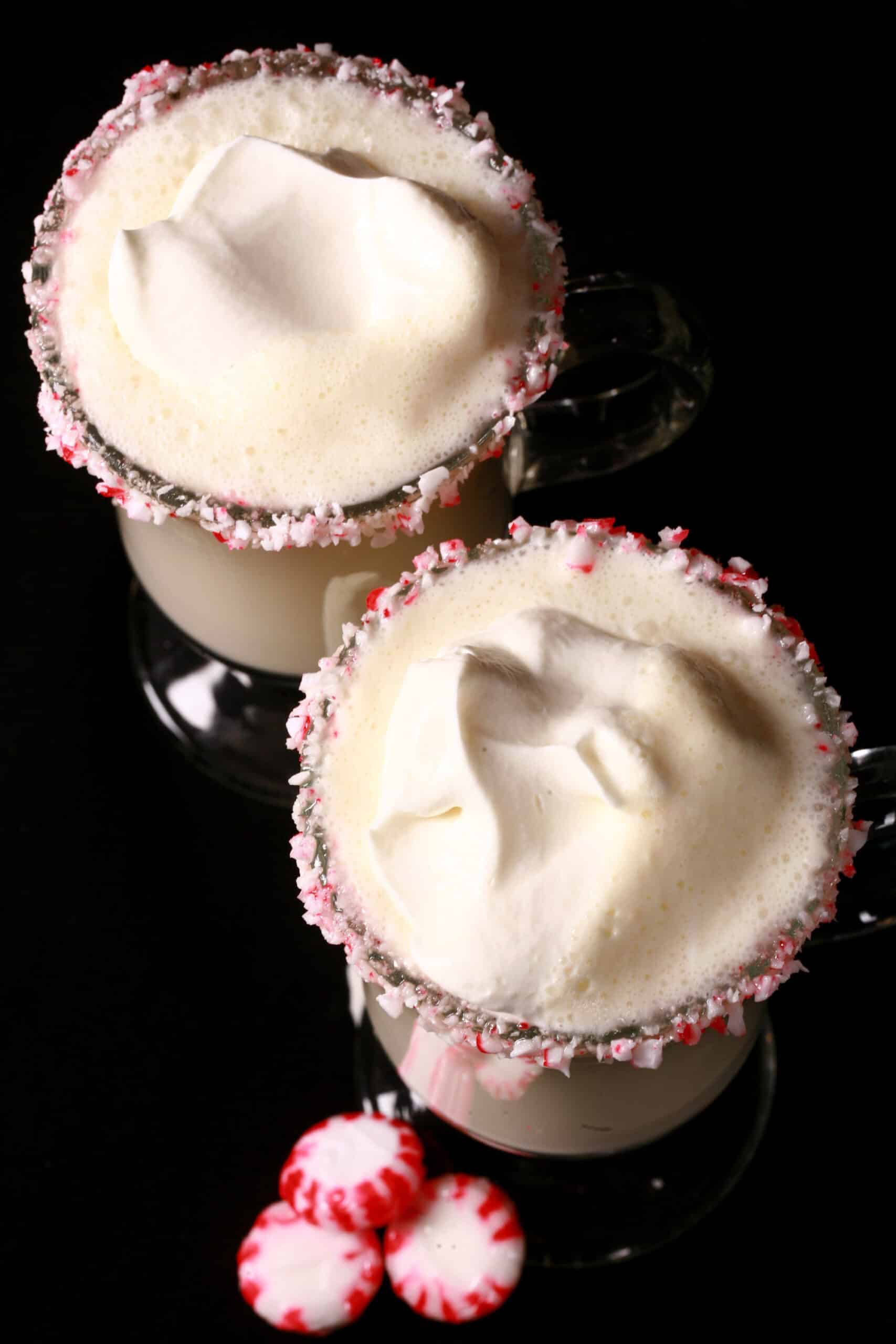 2 mugs of low carb white hot chocolate with rims of sugar free peppermint candy, and topped with whipped cream.