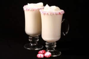 2 mugs of low carb white hot chocolate with rims of sugar free peppermint candy, and topped with whipped cream.