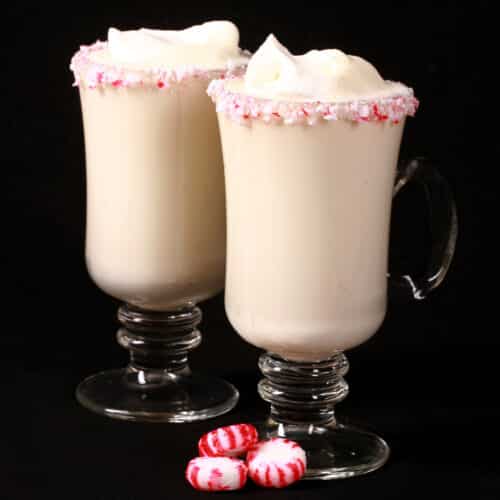 2 mugs of low carb white hot chocolate with rims of sugar free peppermint candy, and topped with whipped cream.