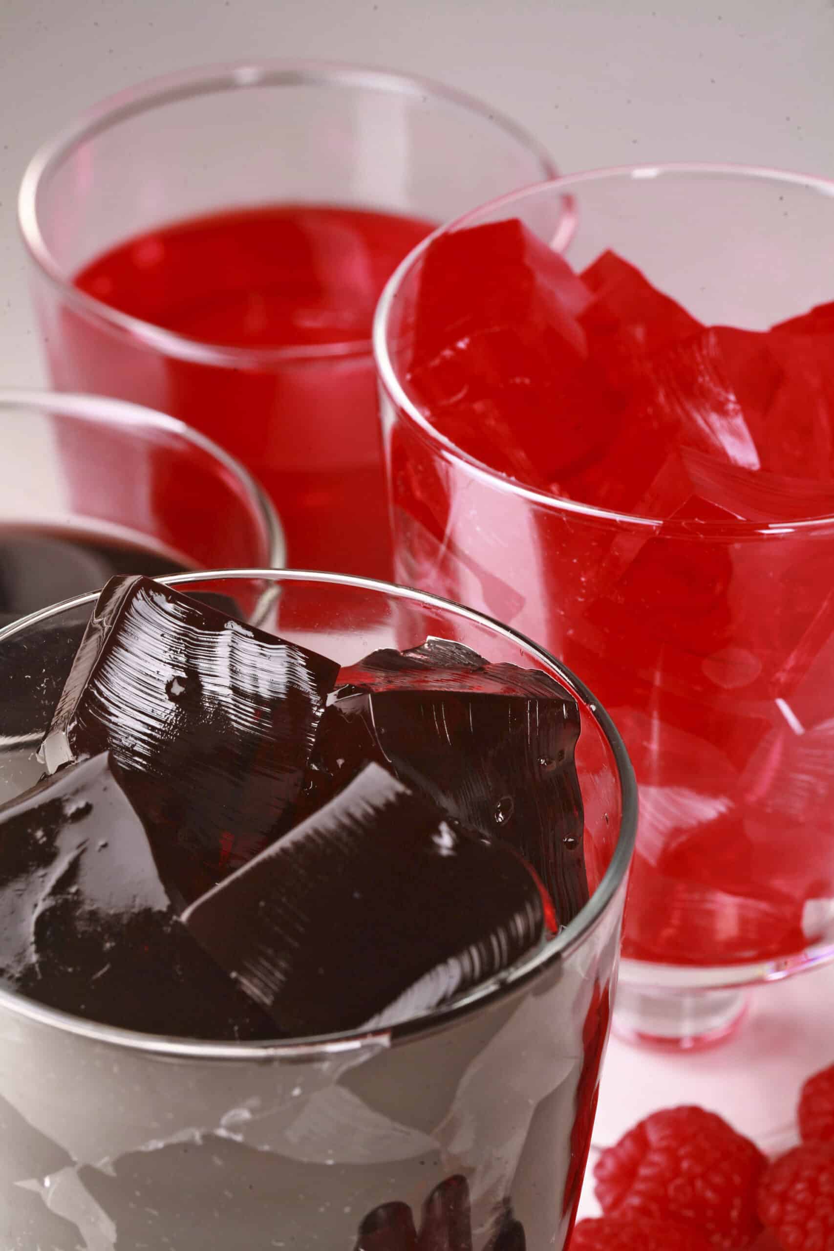 Four glasses of homemade sugar free jello, two red and two purple, with fresh grapes and raspberries at the bases.