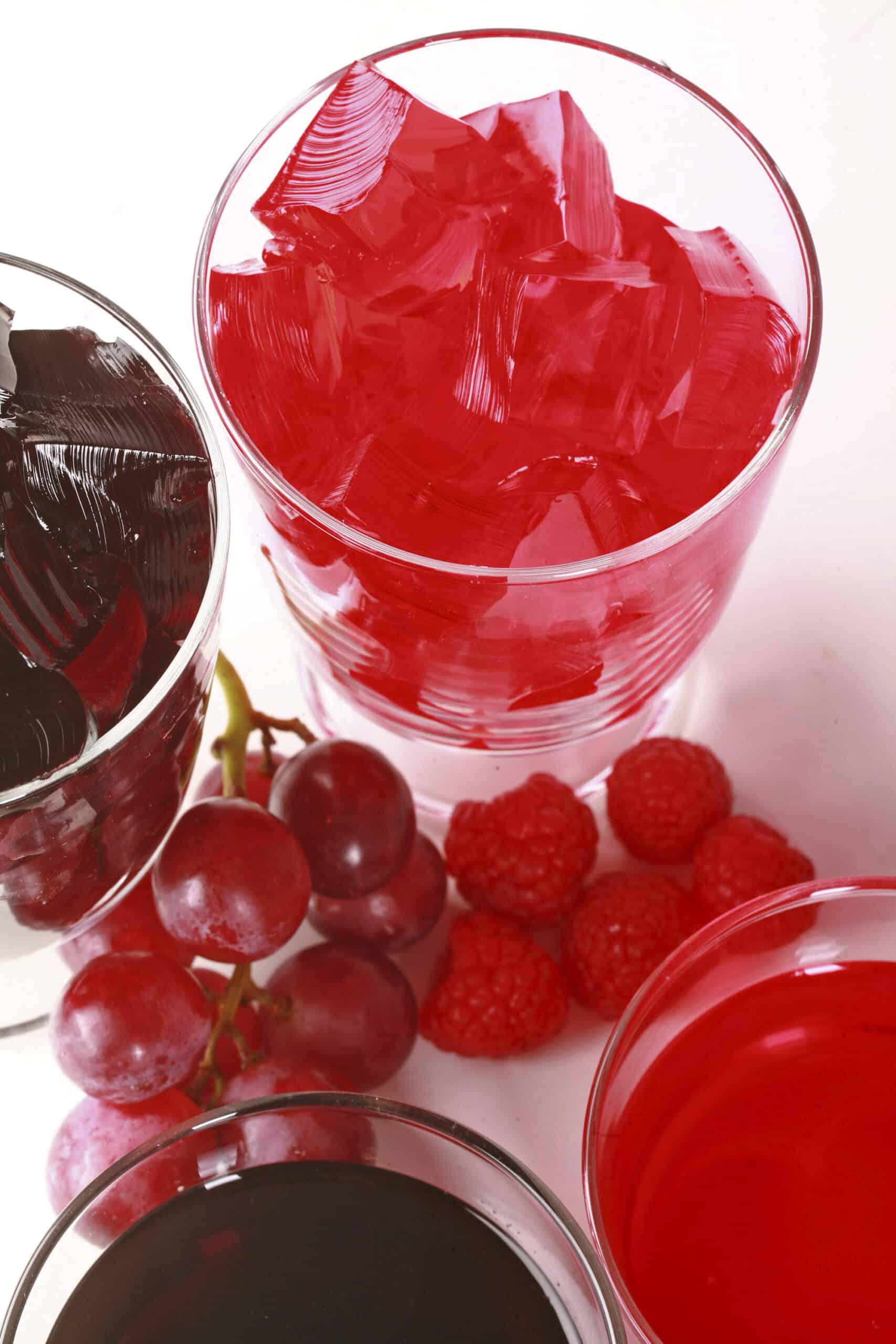 Two glasses of homemade sugar free jello, one red and one purple, with fresh grapes and raspberries at the bases.