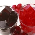 Two glasses of homemade sugar free jello, one red and one purple, with fresh grapes and raspberries at the bases.