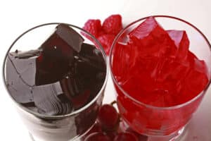 Two glasses of homemade sugar free jello, one red and one purple, with fresh grapes and raspberries at the bases.