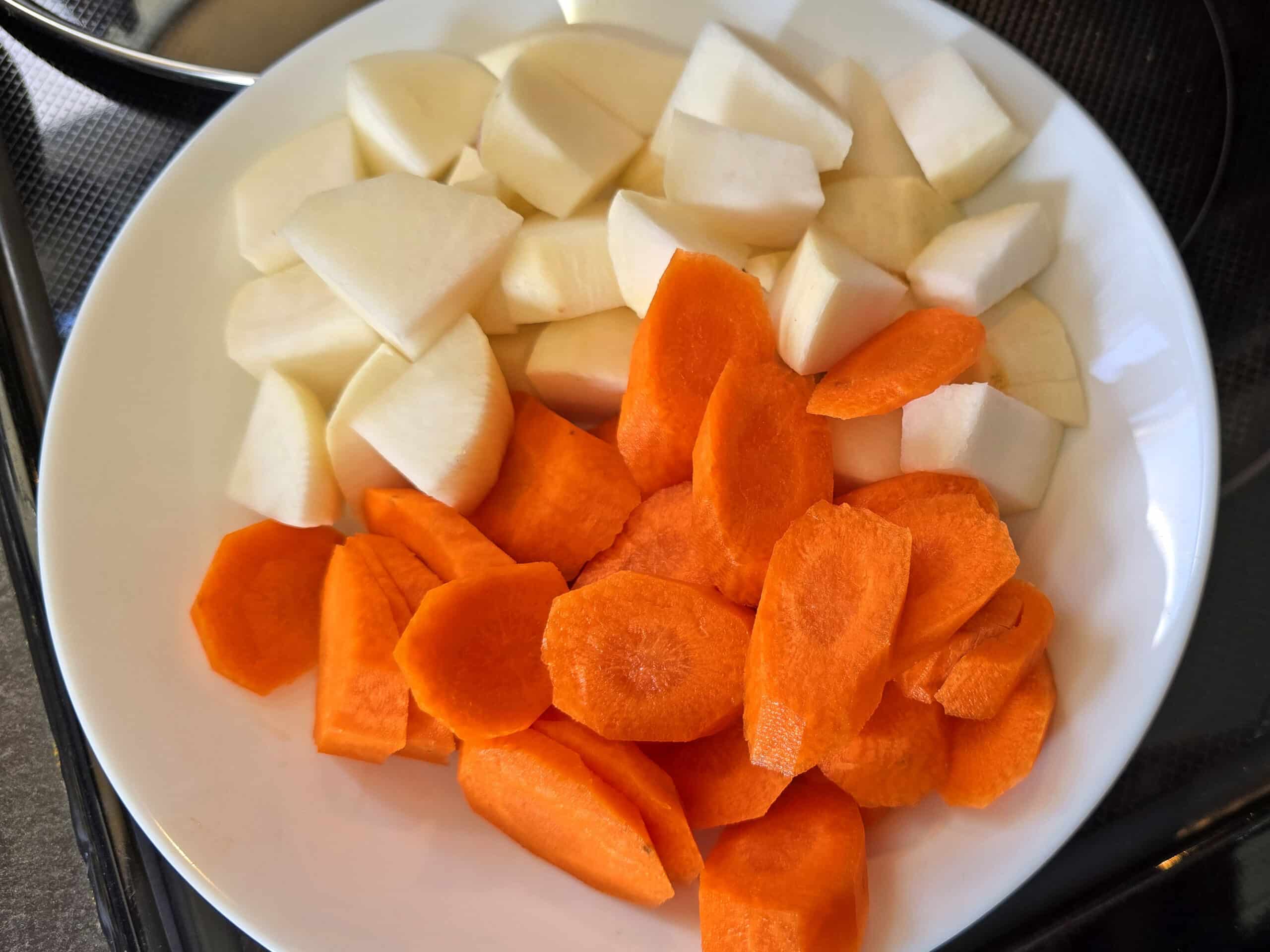 A bowl of sliced carrots and chunks of turnips.