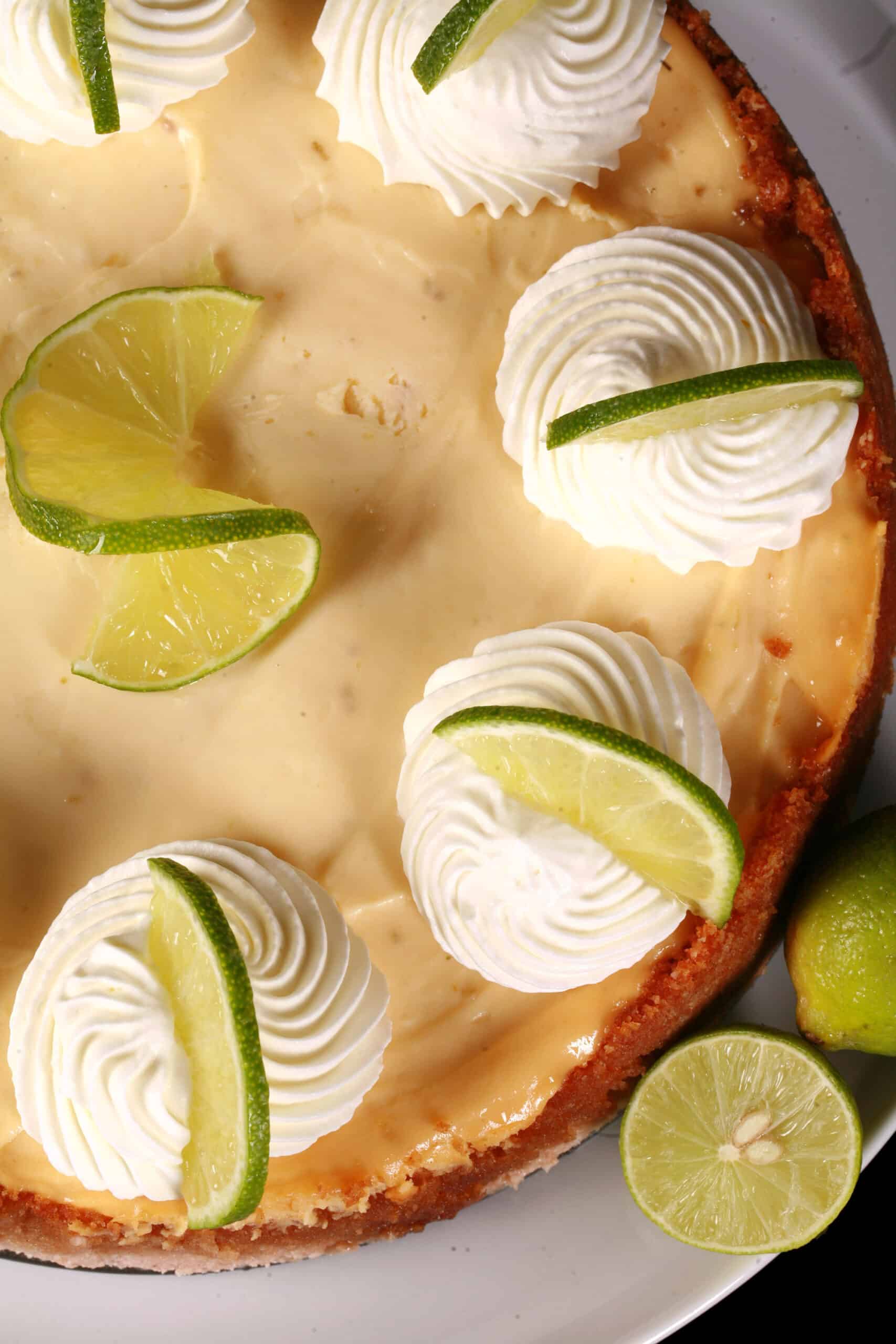 A whole keto key lime cheesecake decorated with swirls of whipped cream and lime slices.