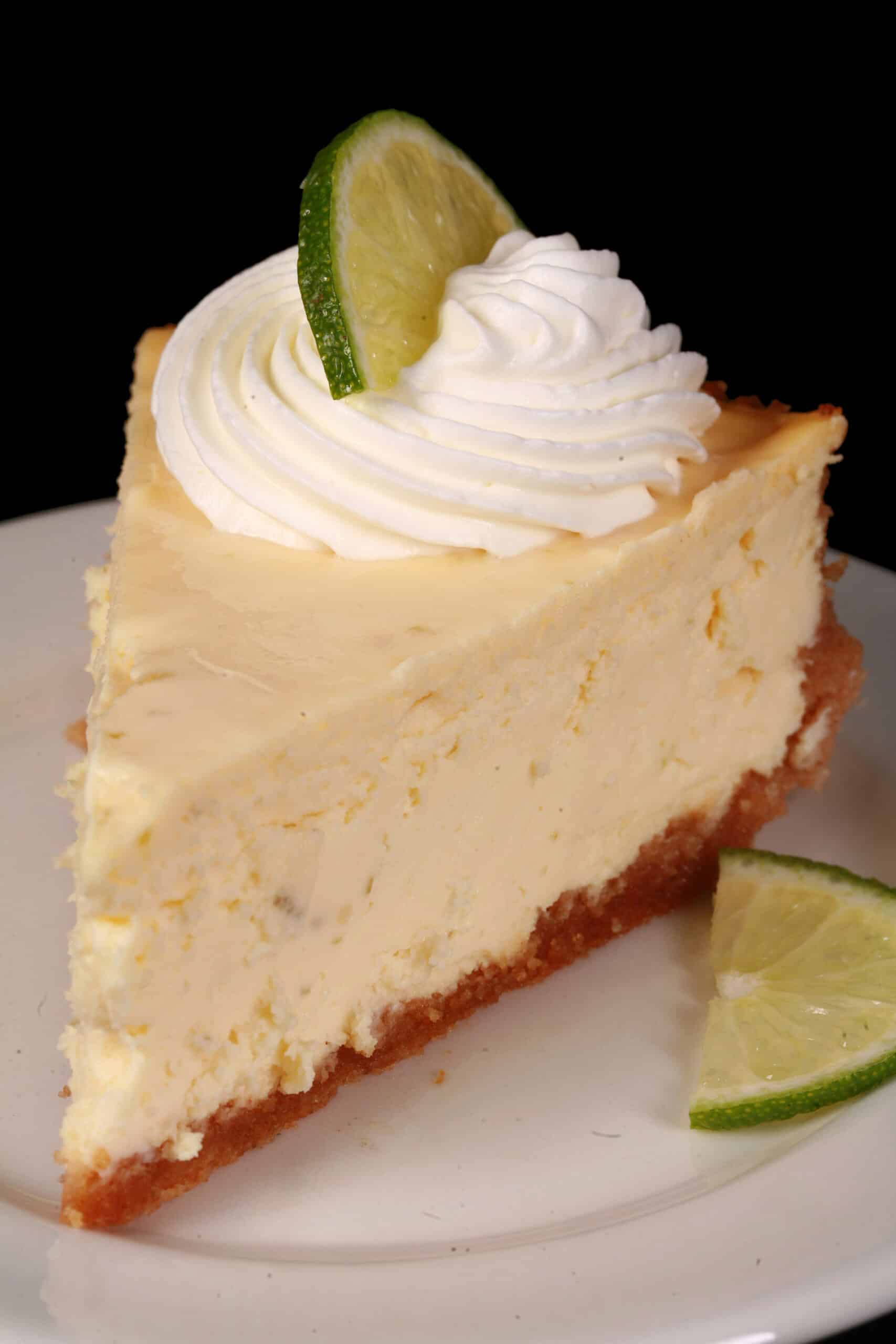 A slice of low carb key lime cheesecake decorated with swirls of whipped cream and lime slices.