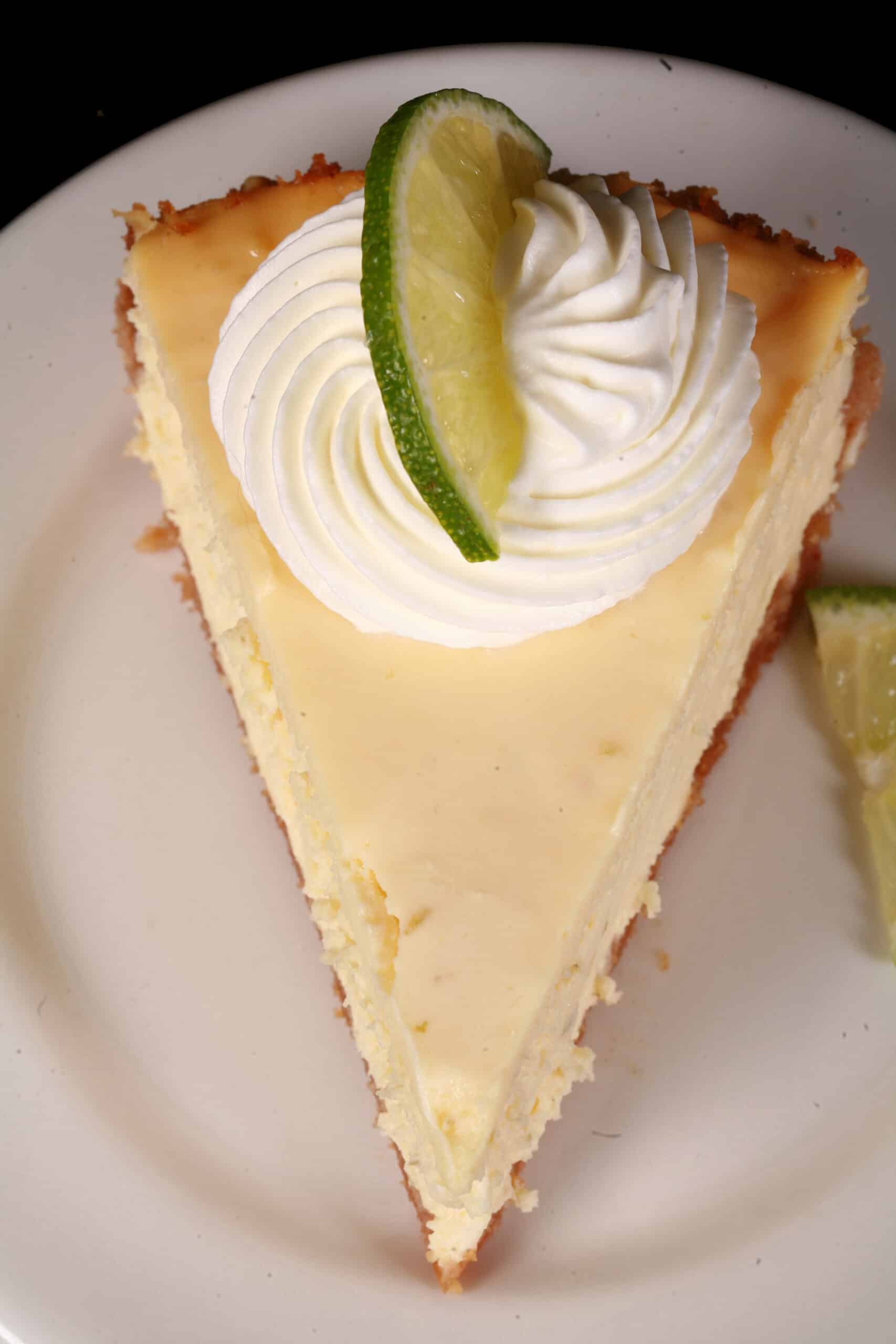 A slice of low carb key lime cheesecake decorated with swirls of whipped cream and lime slices.