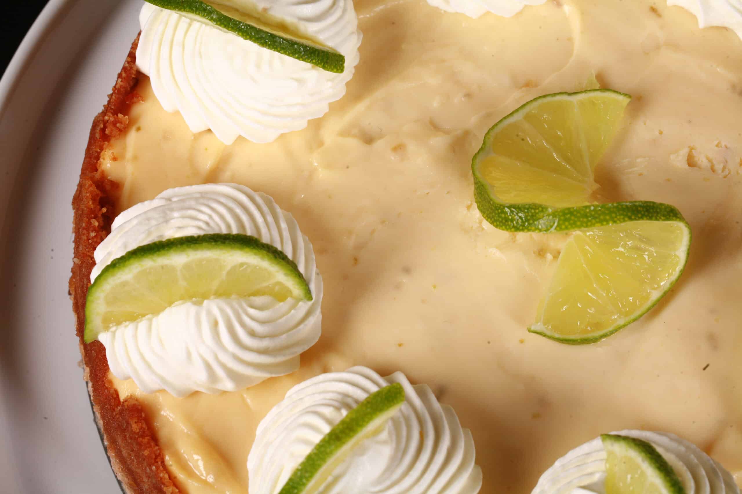 A whole keto key lime cheesecake decorated with swirls of whipped cream and lime slices.