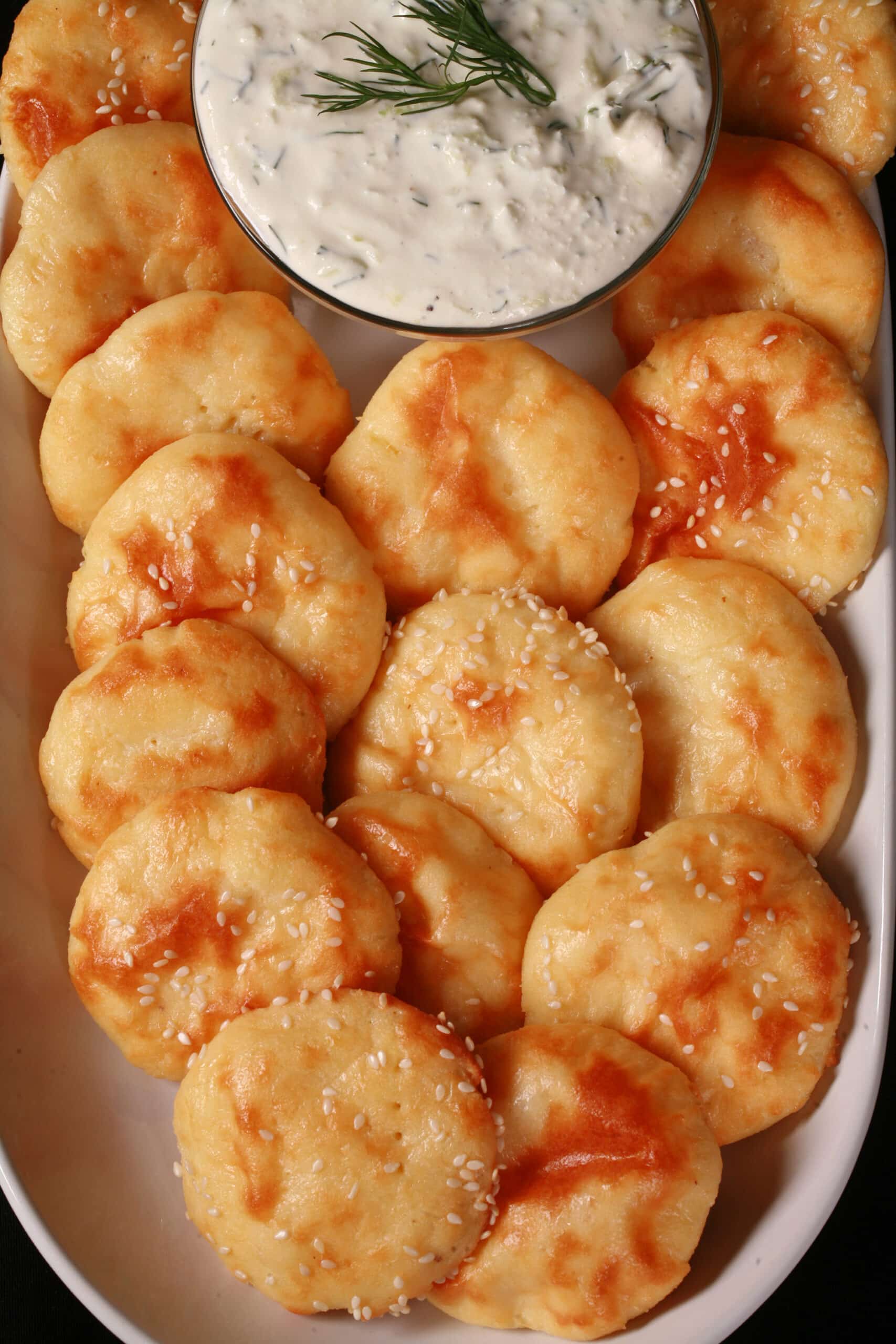 A plate of low carb mini pita rounds with sesame seeds, around a bowl of dip.