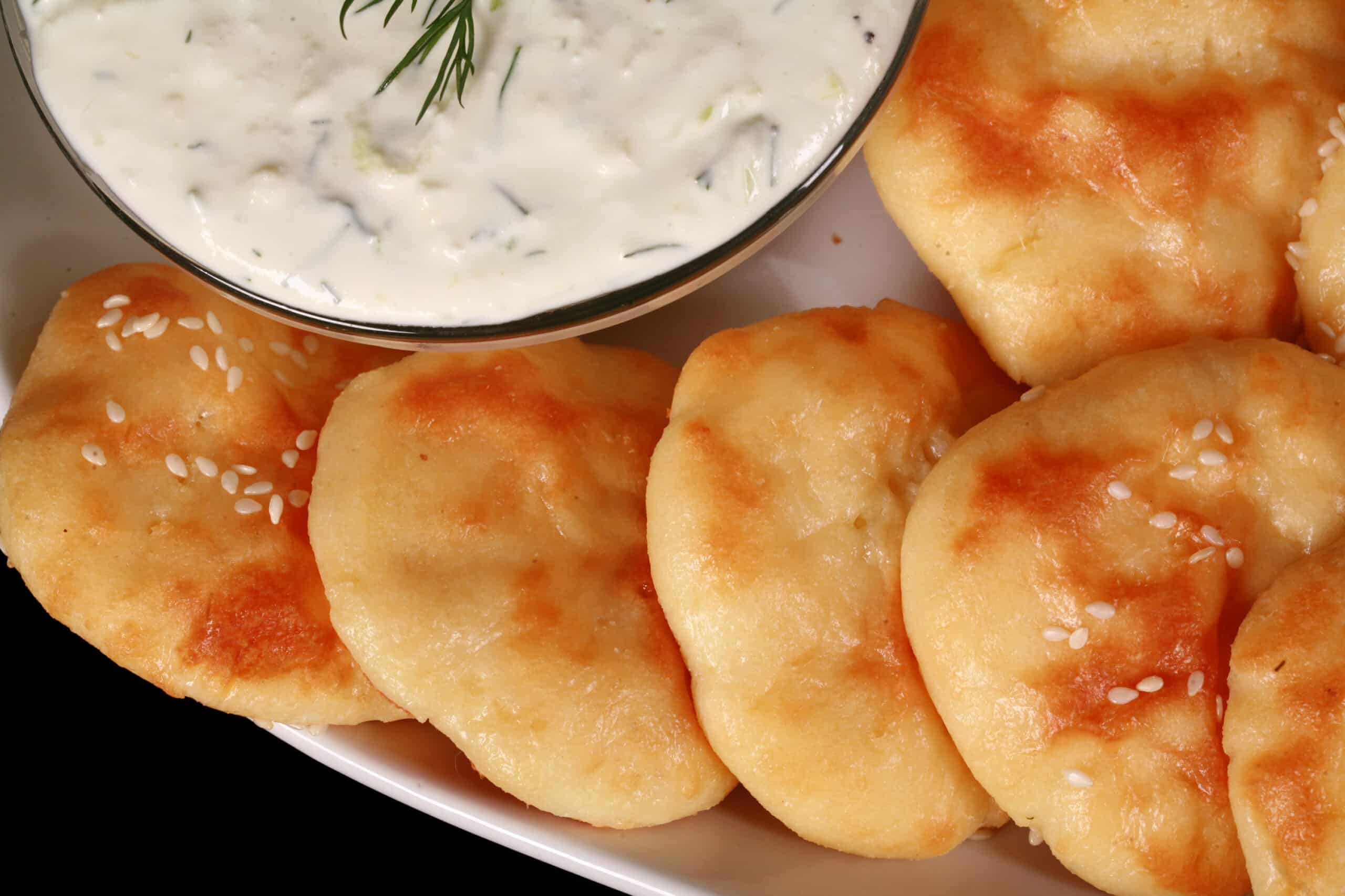 A plate of keto mini pita rounds with sesame seeds, around a bowl of dip.