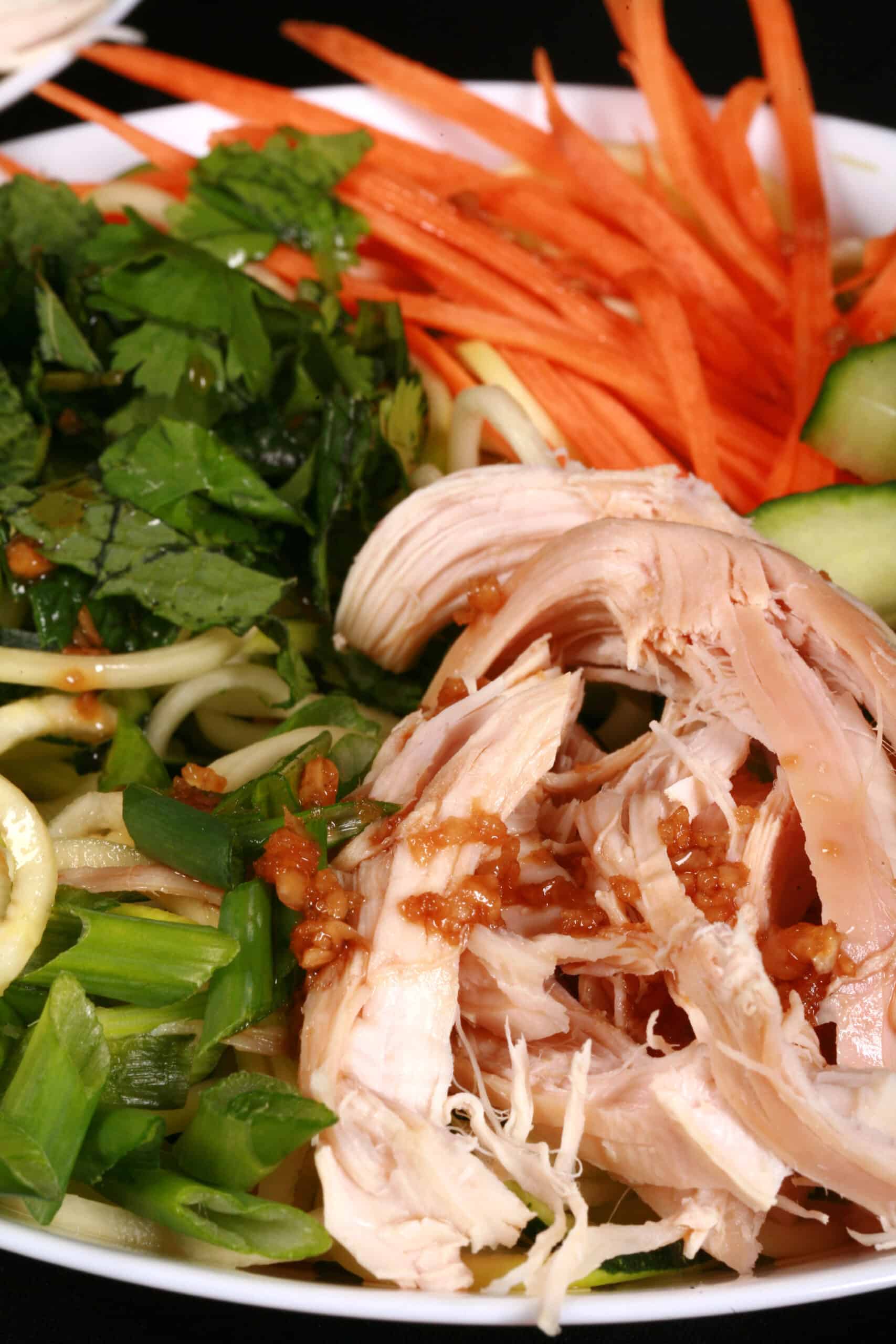 Two bowls of Vietnamese zoodle salads, with zucchini noodles, cucumber, carrot, mint, cilantro, chicken, and dressing.