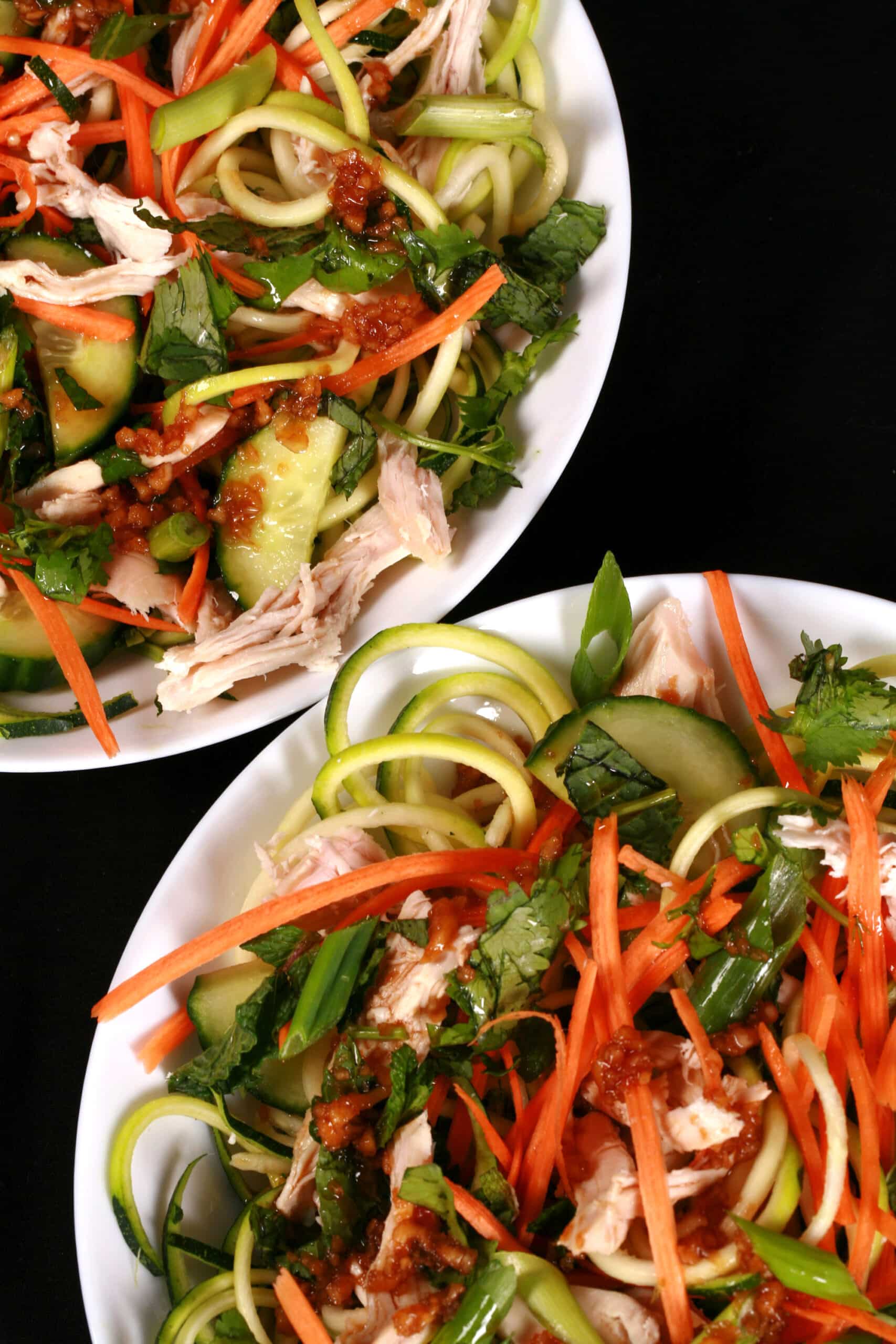 Two bowls of Vietnamese zucchini noodle salads, with zoodles, cucumber, carrot, mint, cilantro, chicken, and dressing.