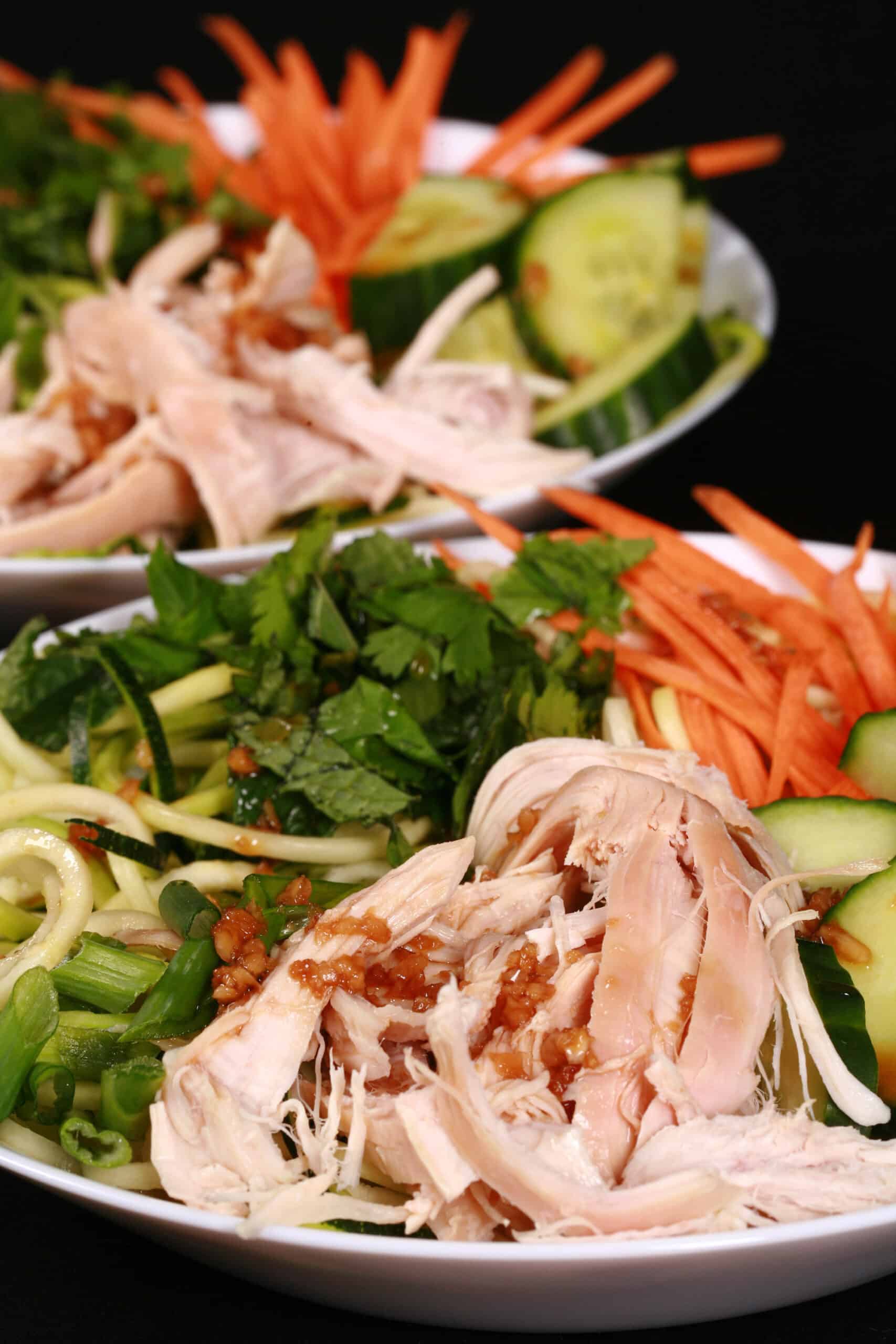 Two bowls of Vietnamese zoodle salads, with zucchini noodles, cucumber, carrot, mint, cilantro, chicken, and dressing.