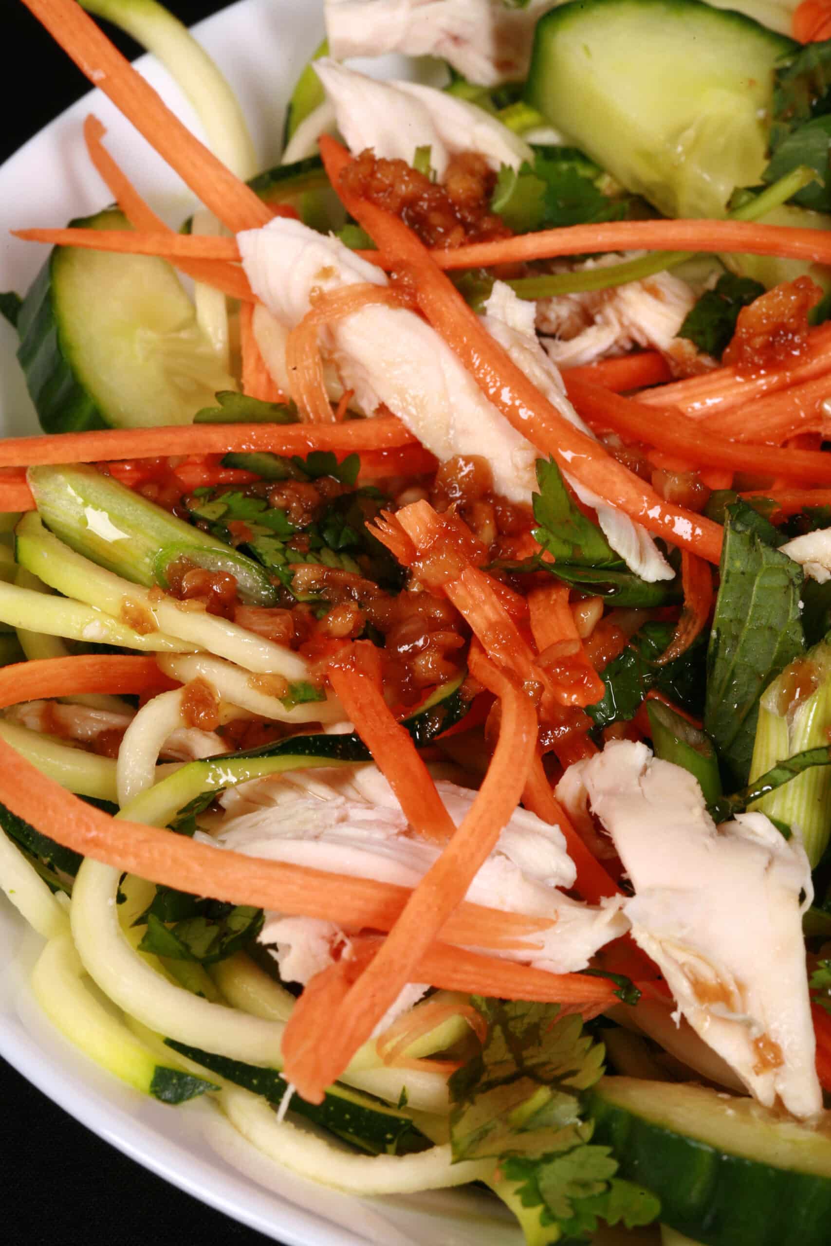 Two bowls of Vietnamese zucchini noodle salads, with zoodles, cucumber, carrot, mint, cilantro, chicken, and dressing.