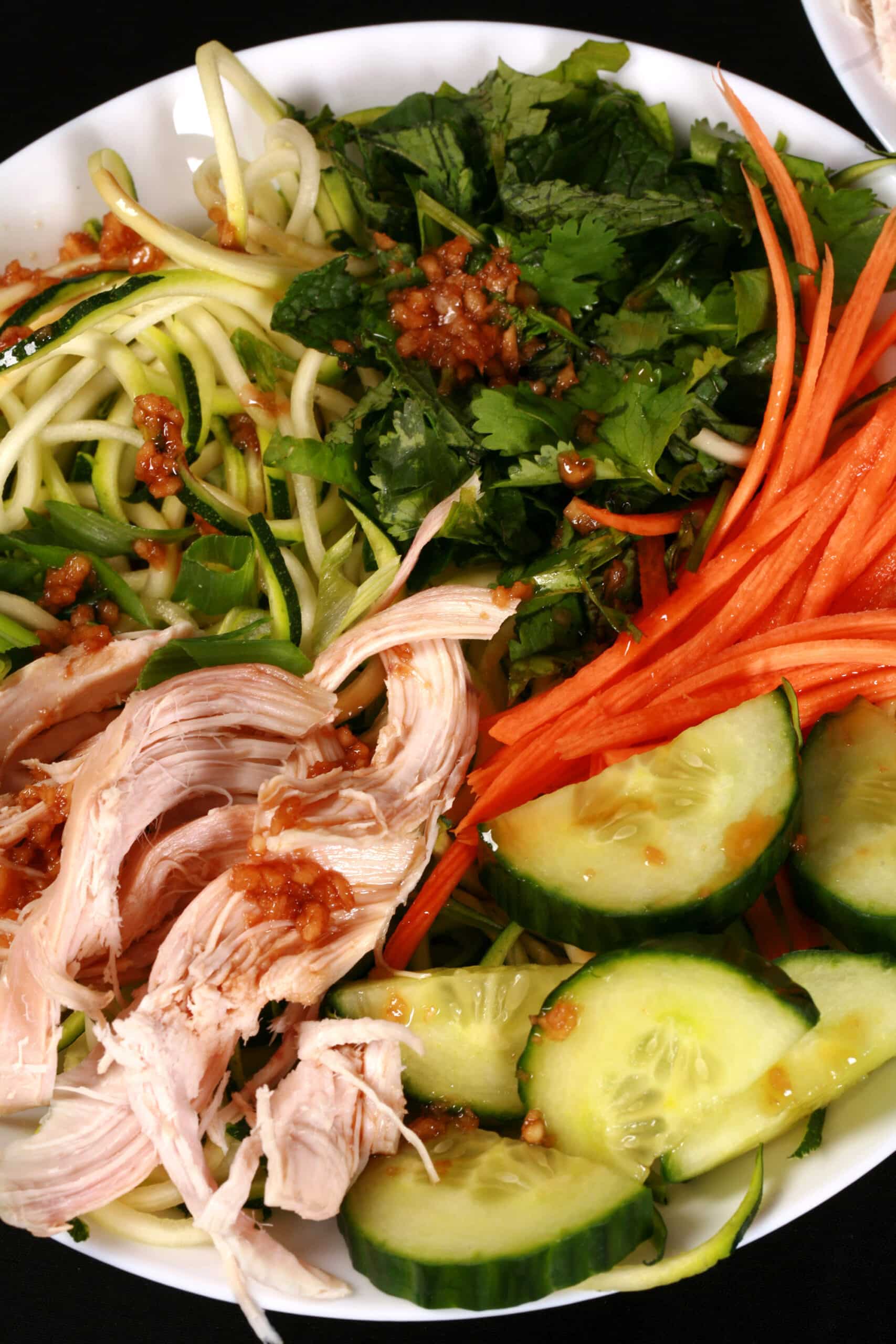 Two bowls of Vietnamese zoodle salads, with zucchini noodles, cucumber, carrot, mint, cilantro, chicken, and dressing.