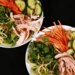 Two bowls of Vietnamese zucchini noodle salads, with zoodles, cucumber, carrot, mint, cilantro, chicken, and dressing.
