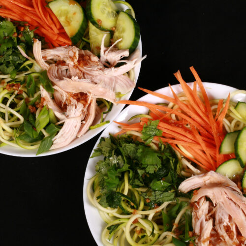 Two bowls of Vietnamese zucchini noodle salads, with zoodles, cucumber, carrot, mint, cilantro, chicken, and dressing.